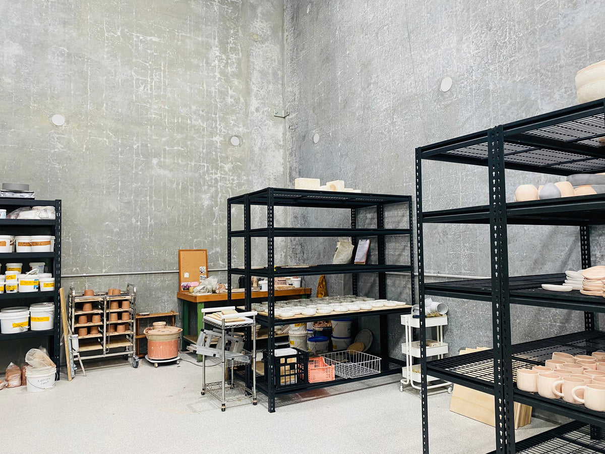 Rhiannon Gill's new studio, concrete walls and black shelving stacked with unglazed ceramics