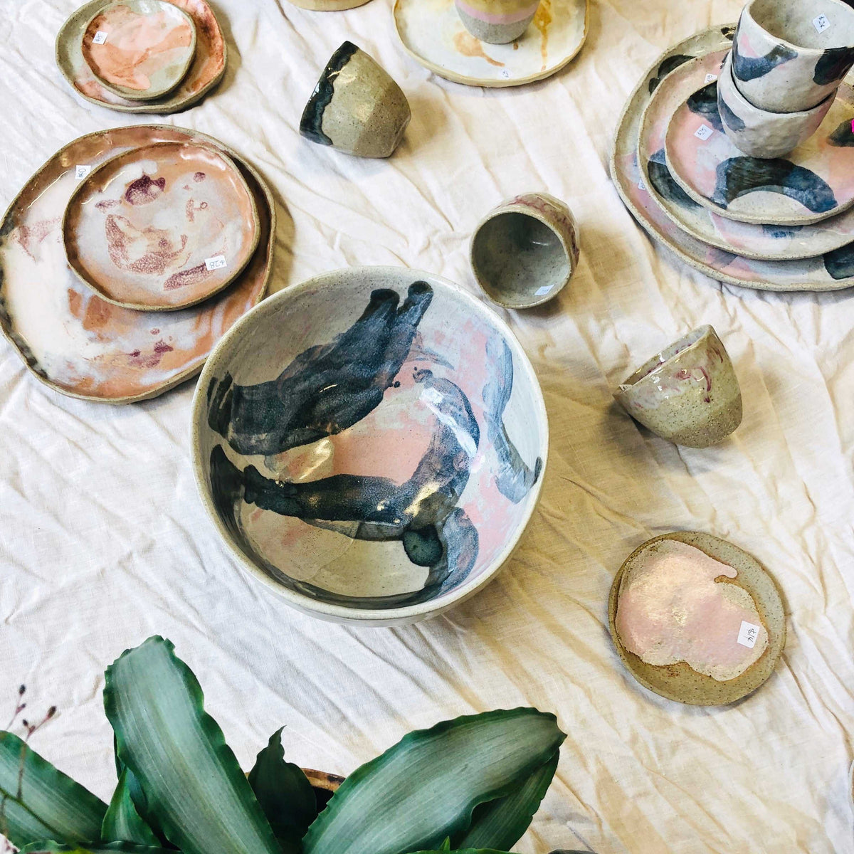Handmade ceramic bowls, plates and cups in pink, navy and cream laid out on a white cloth
