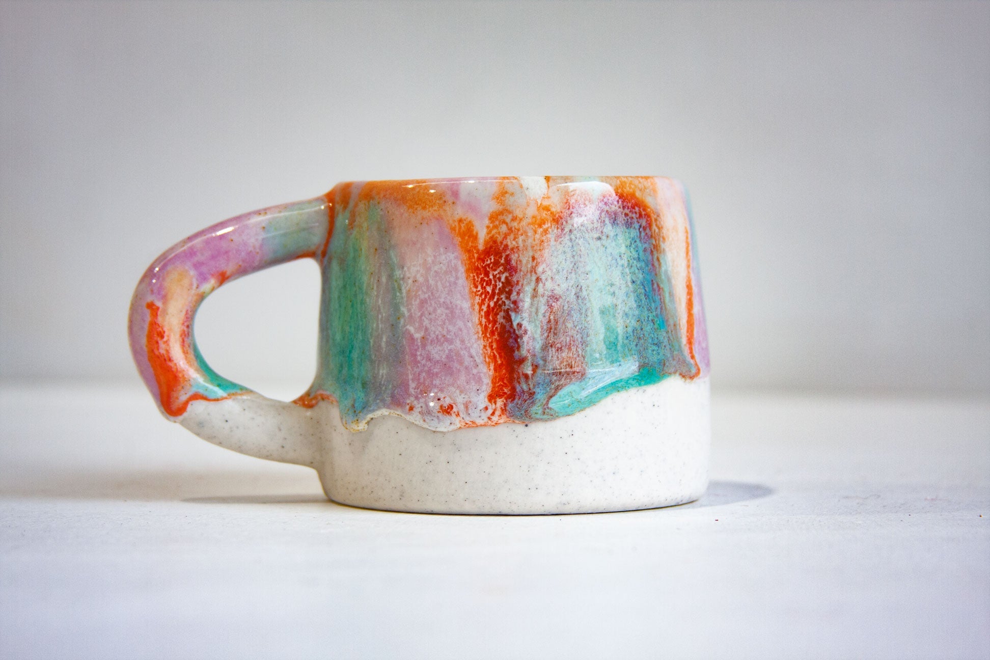 Two handmade ceramic espresso cups stacked at an angle, showing lilac and orange glaze with purple drips over speckled white stoneware
