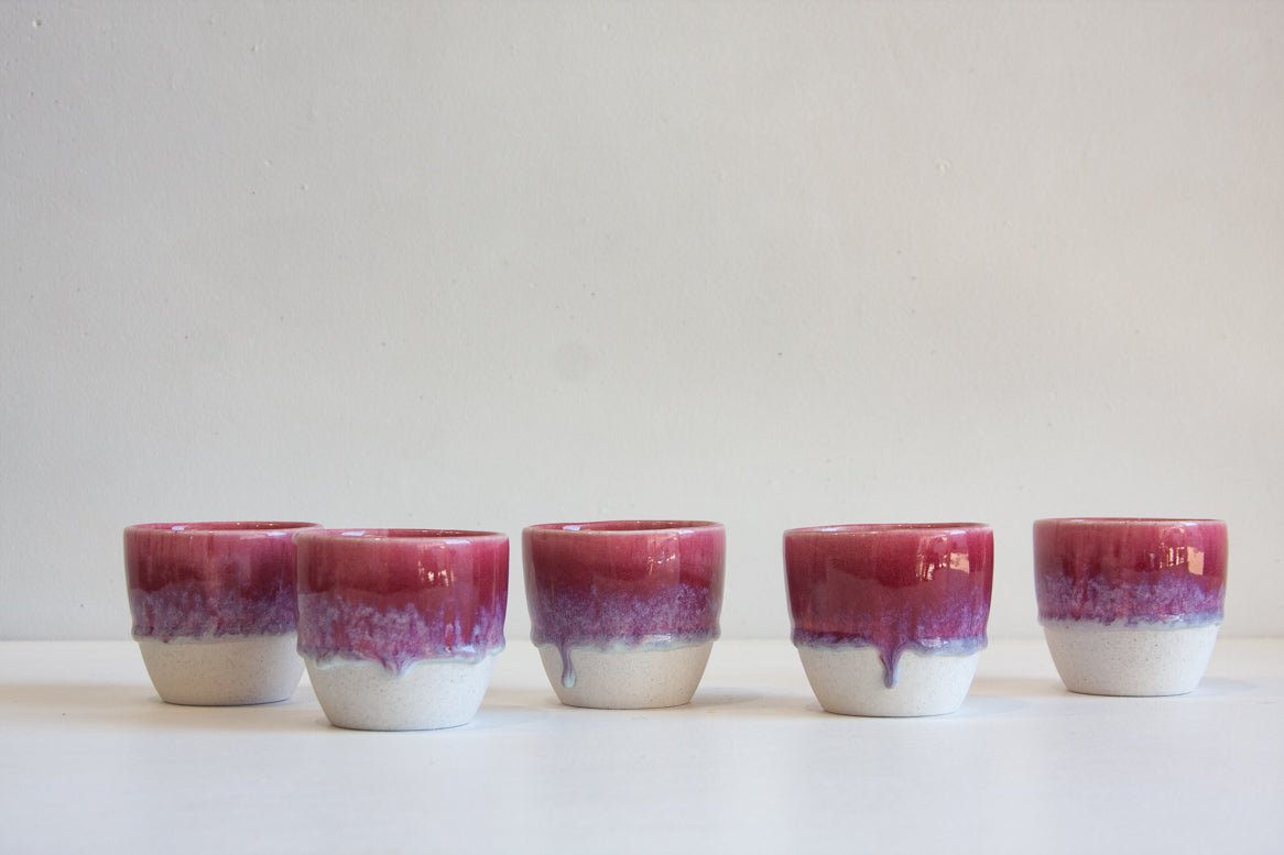 handmade ceramic espresso cup at an angle, showing lilac and orange glaze with purple drips over speckled white stoneware