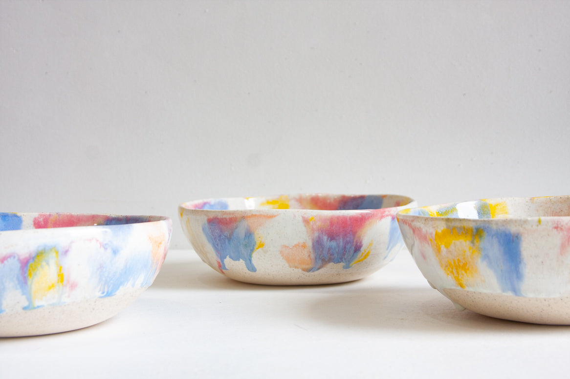 Three handmade ceramic pasta bowls in a row, brush-glazed in blue, pink and yellow