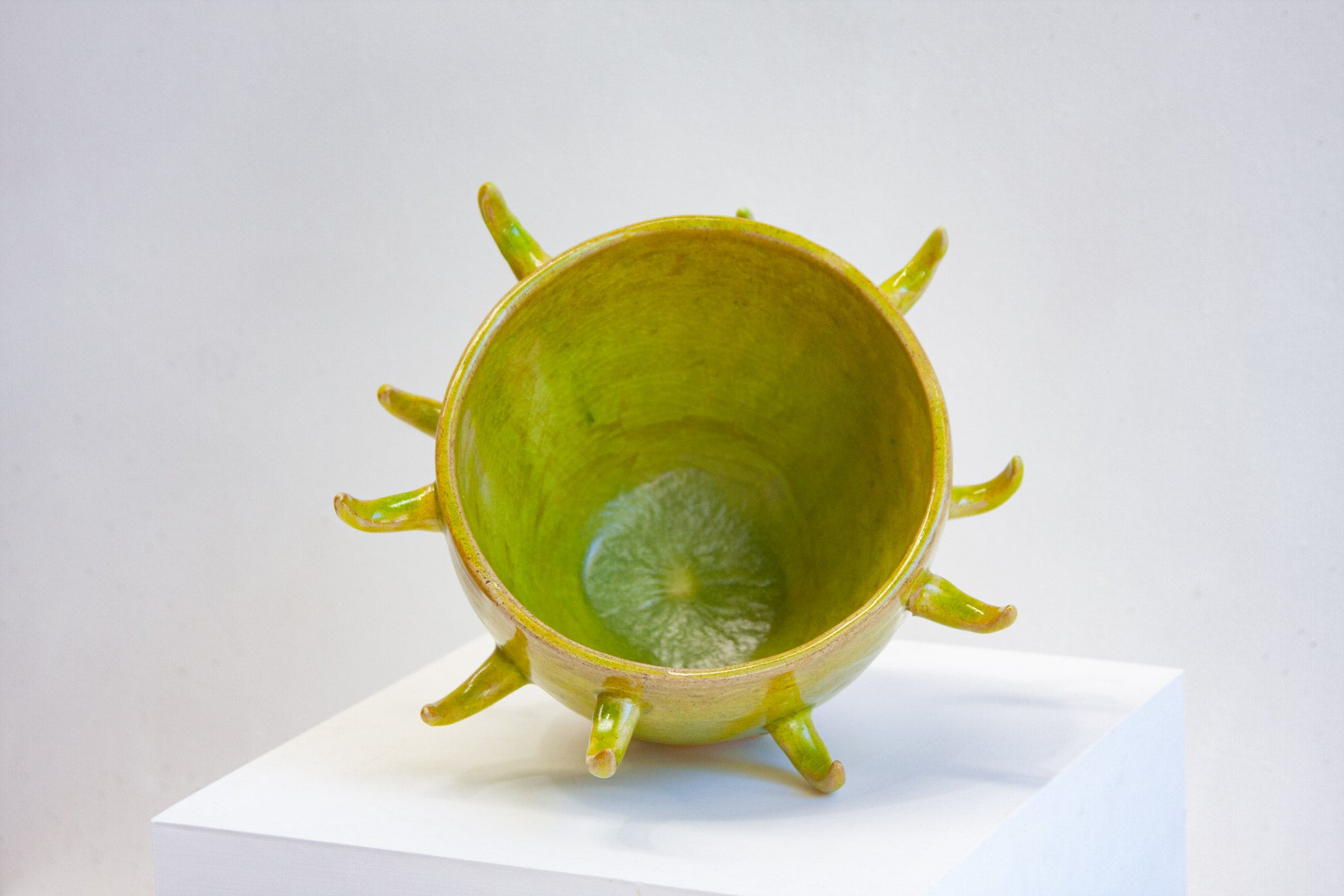 Looking down into a handmade ceramic spiked vessel, the acid green glaze pooling in the base and clay horns curling out around the rim.
