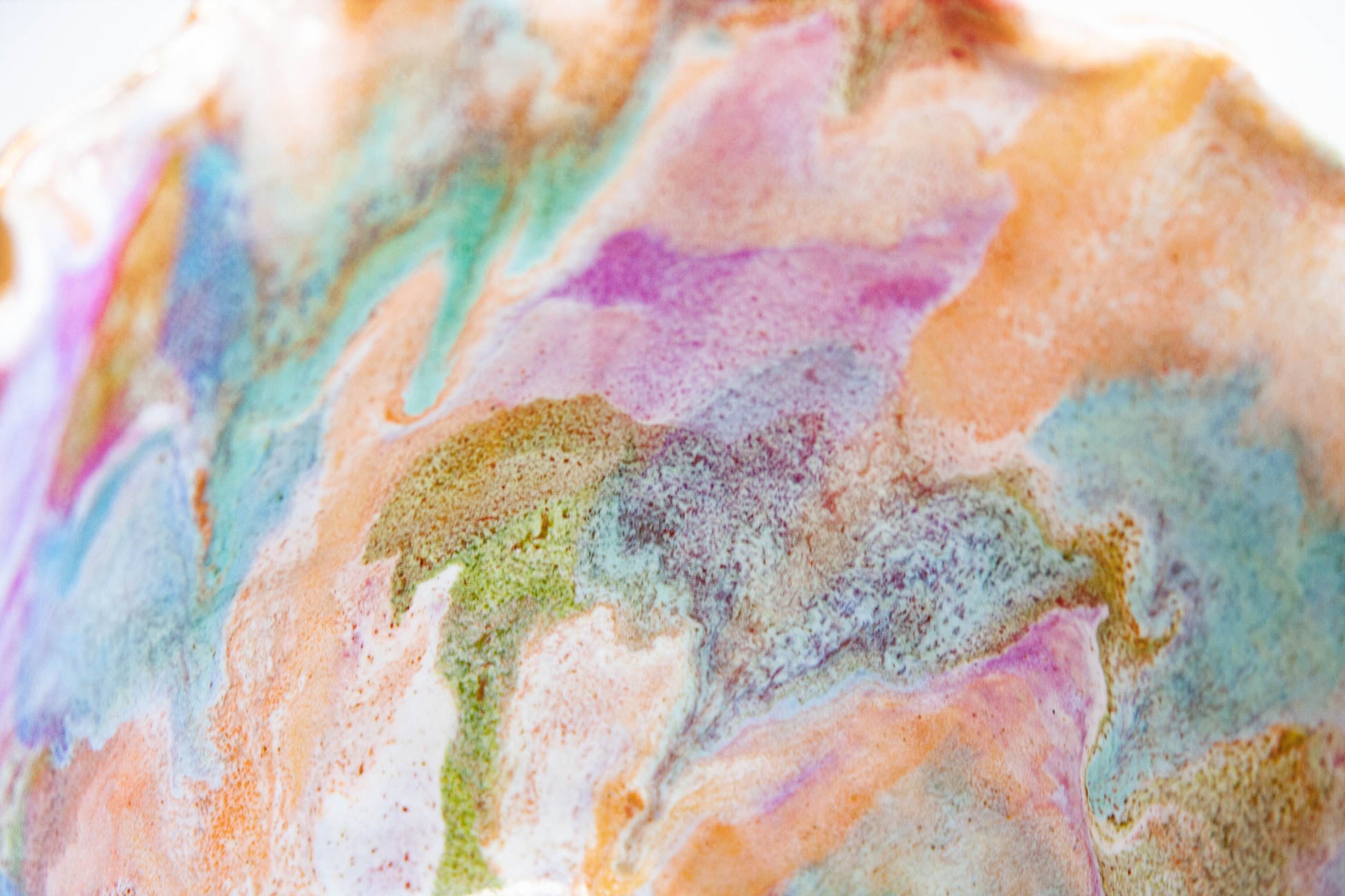 Close-up of the glaze on a handmade ceramic frill vessel, peach, pink, blue and green washing into each other over white.