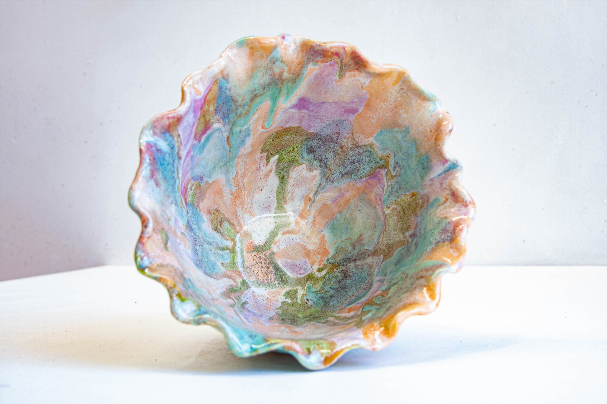 Looking down into a handmade ceramic frill vessel, the glazed interior swirling through green, peach, blue and purple inside the frilled rim.