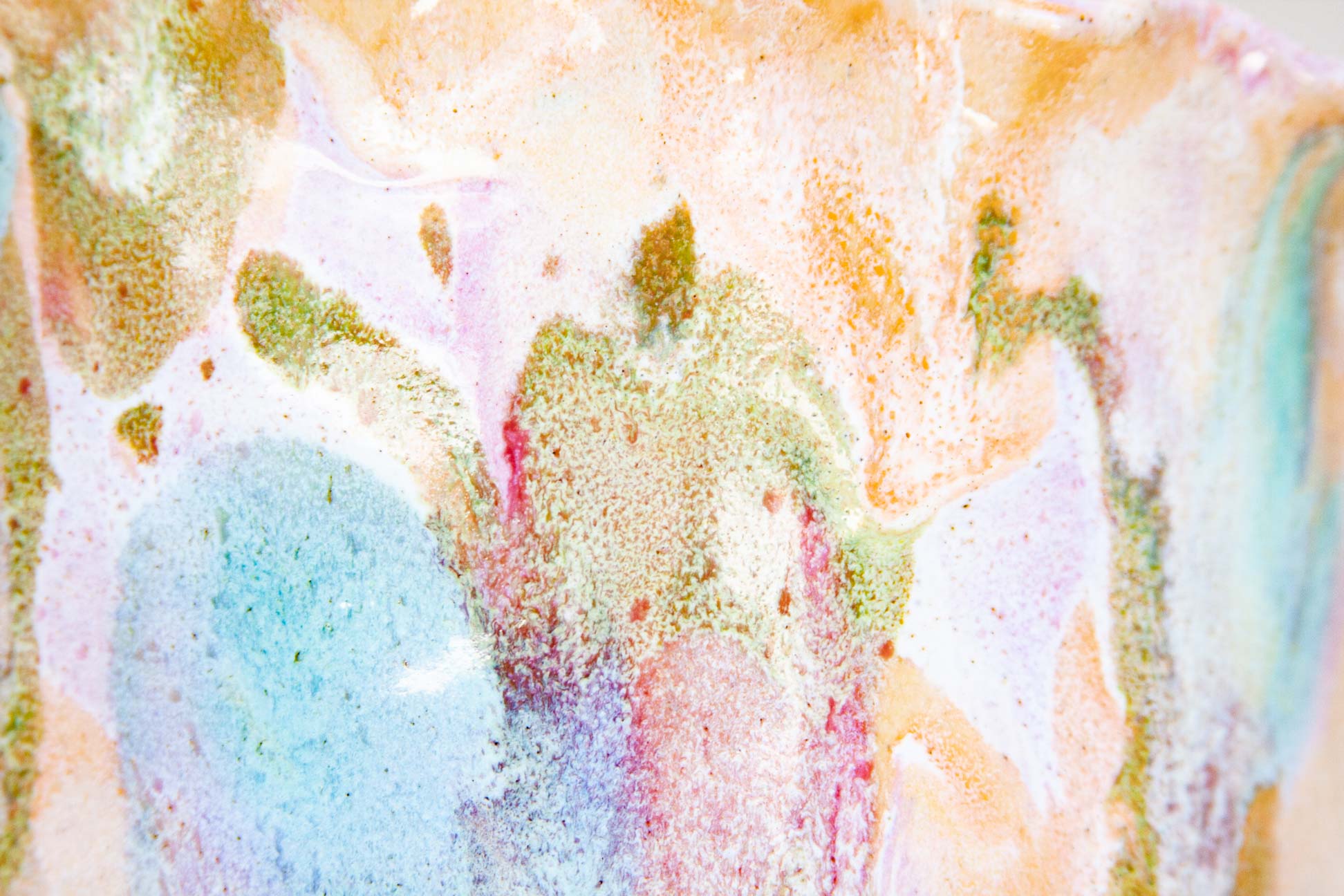 Close-up of the glaze on a handmade ceramic frill vessel, a pool of blue sitting among green, peach and pink over white.