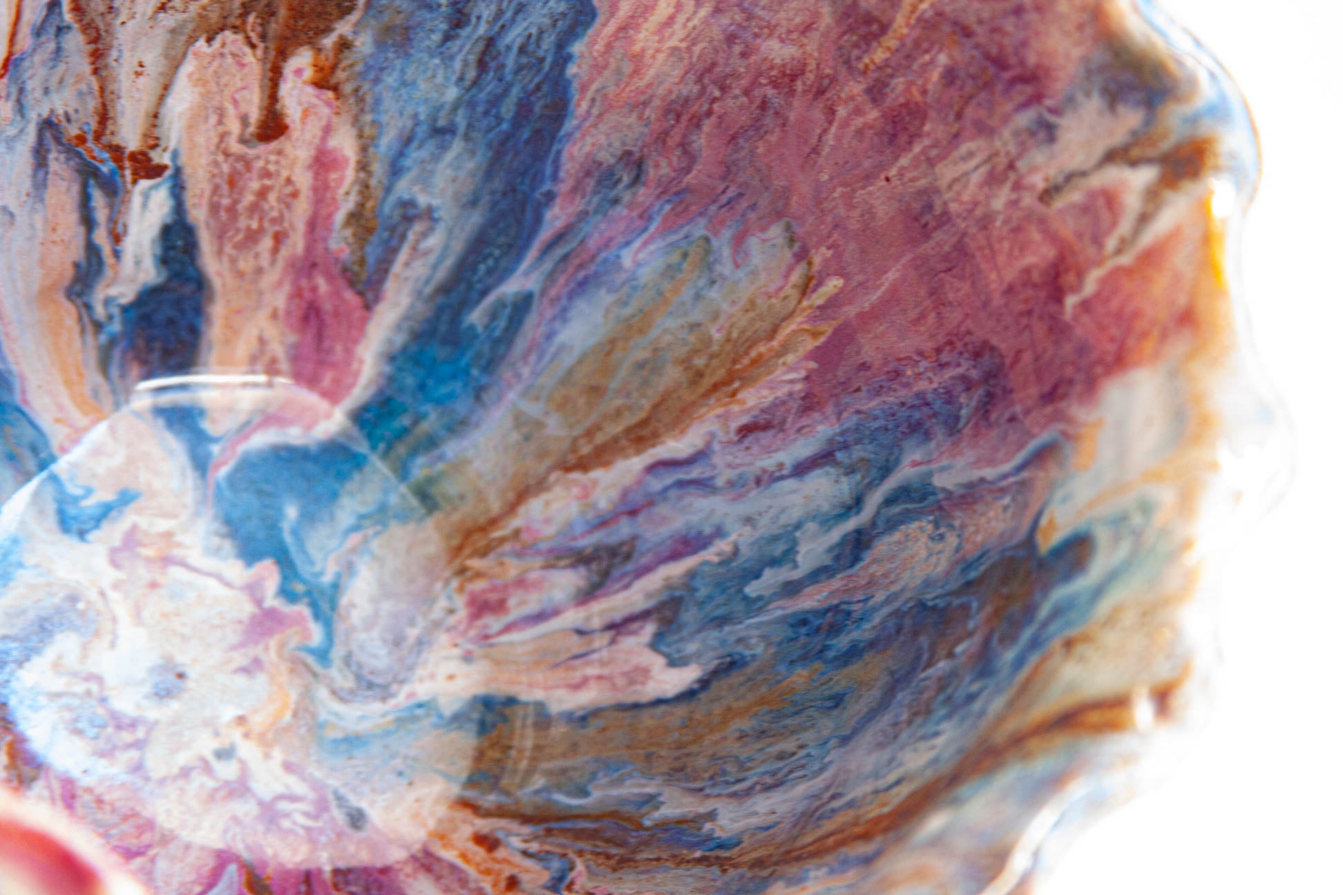 Close-up inside a handmade ceramic frill vessel, the glaze swirling through pink, blue, rust and white across the glazed interior.