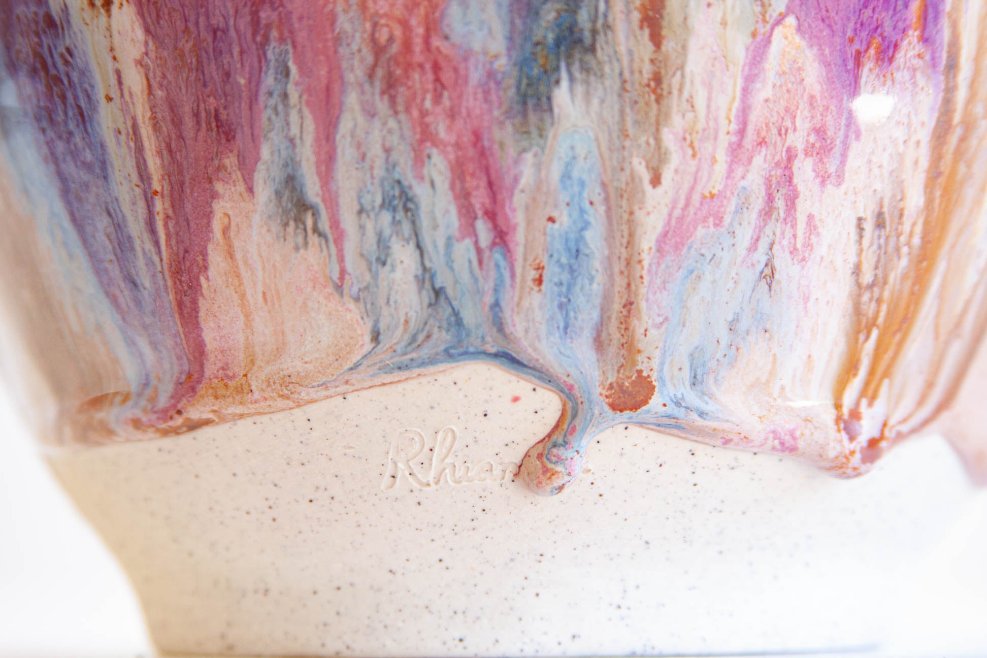 Close-up of the foot of a handmade ceramic frill vessel, the glaze ending above bare white clay stamped with the maker's mark.