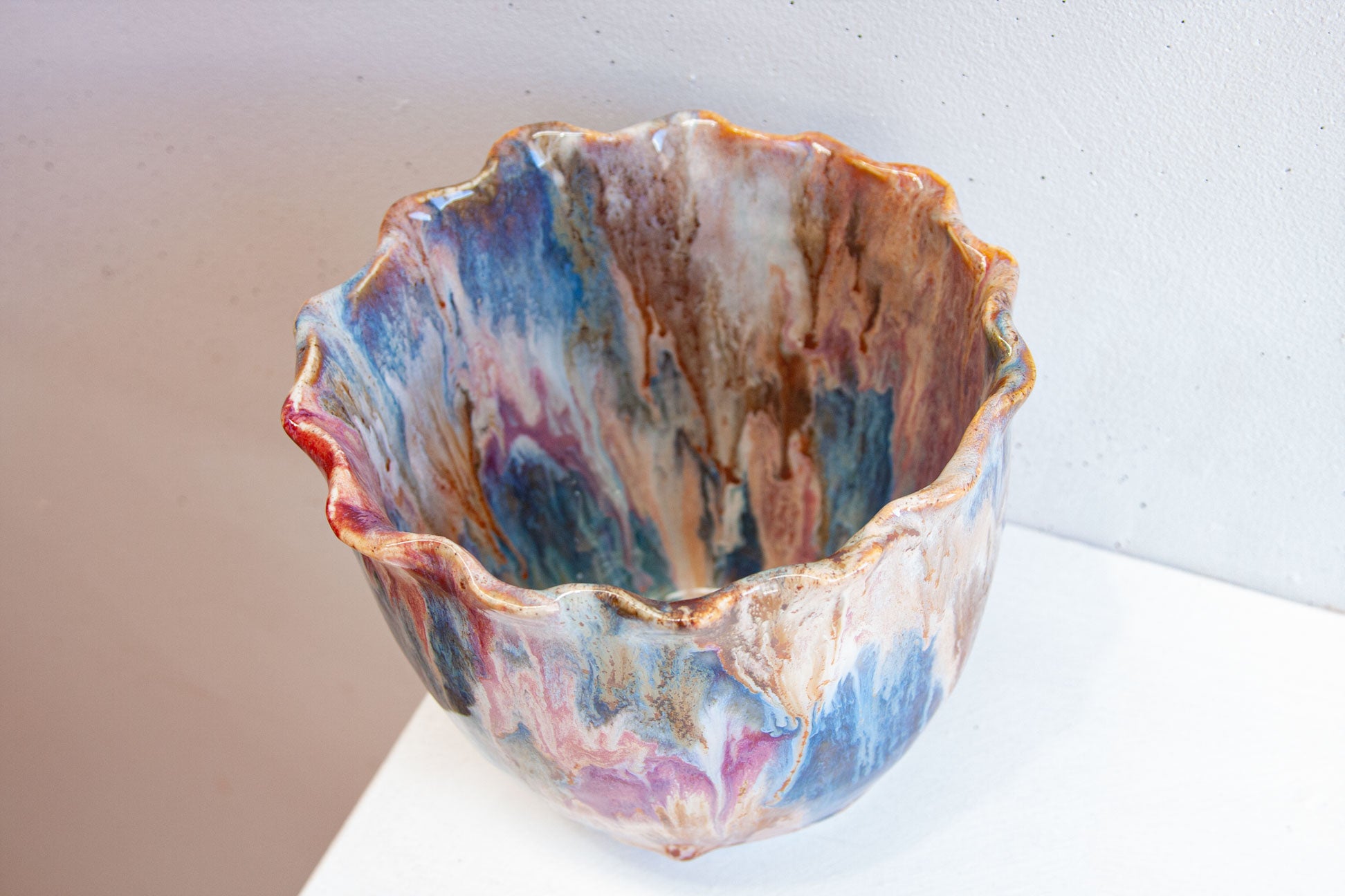 Looking down into a handmade ceramic frill vessel, the glazed interior running through brown, pink, blue and white inside the frilled rim.