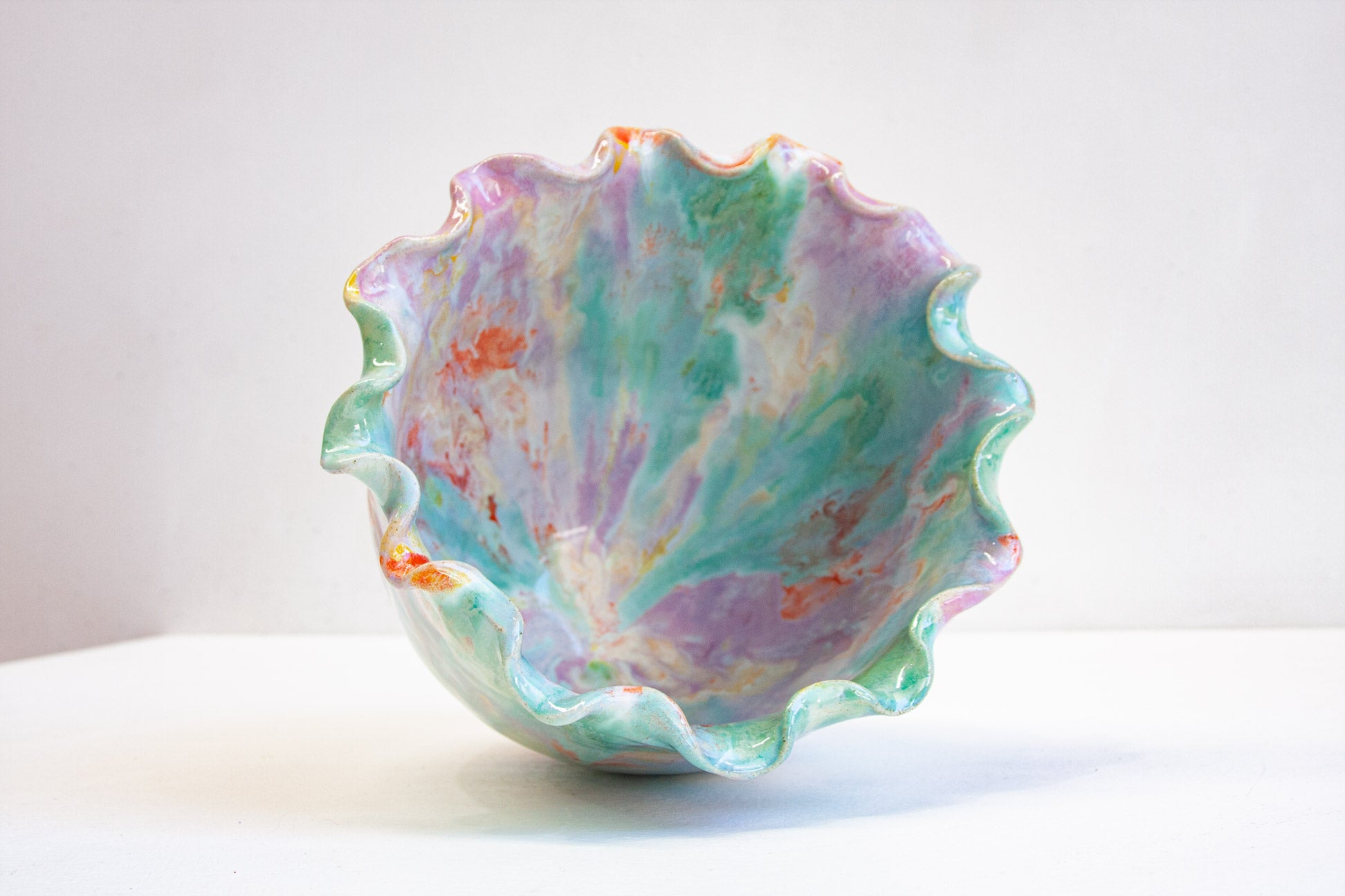 Looking down into a handmade ceramic frill vessel, the glazed interior washing through purple, green and orange inside the frilled rim.