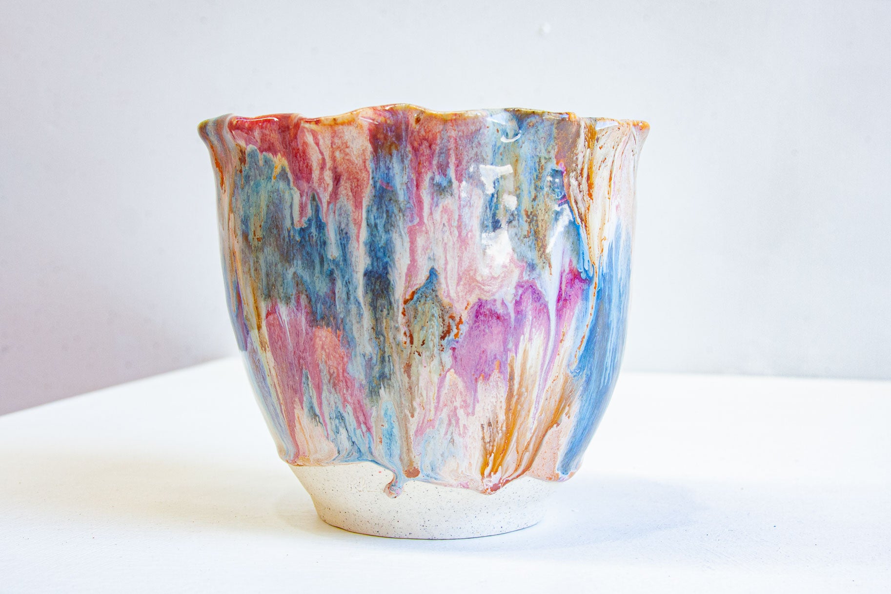 A handmade ceramic frill vessel seen from the front, brown, pink and blue running down the flared sides to a bare white clay foot.