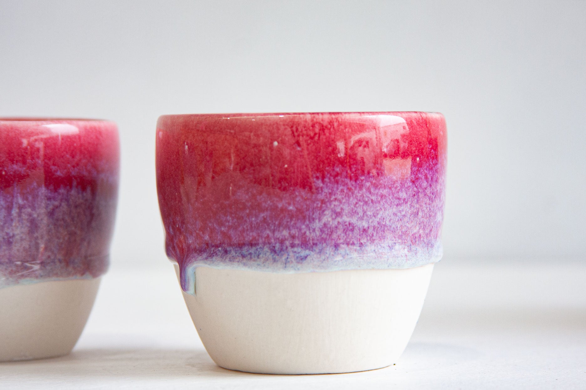 Close-up of a handmade ceramic cup, the deep pink glaze running into violet speckle and ending in a clean line above the bare white clay.