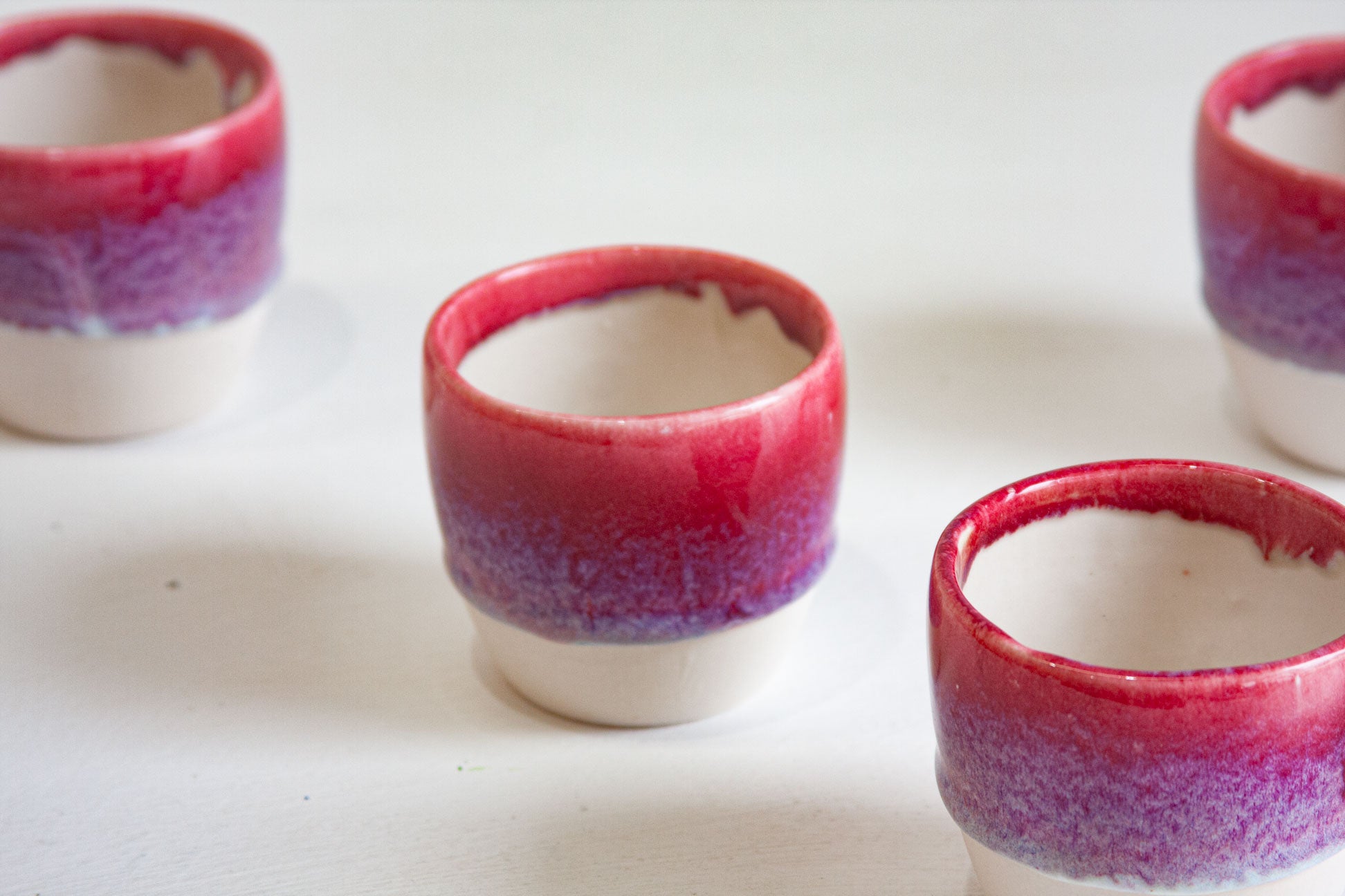 Four handmade ceramic cups seen from above, showing the white glazed interiors and the deep pink rims fading into violet.