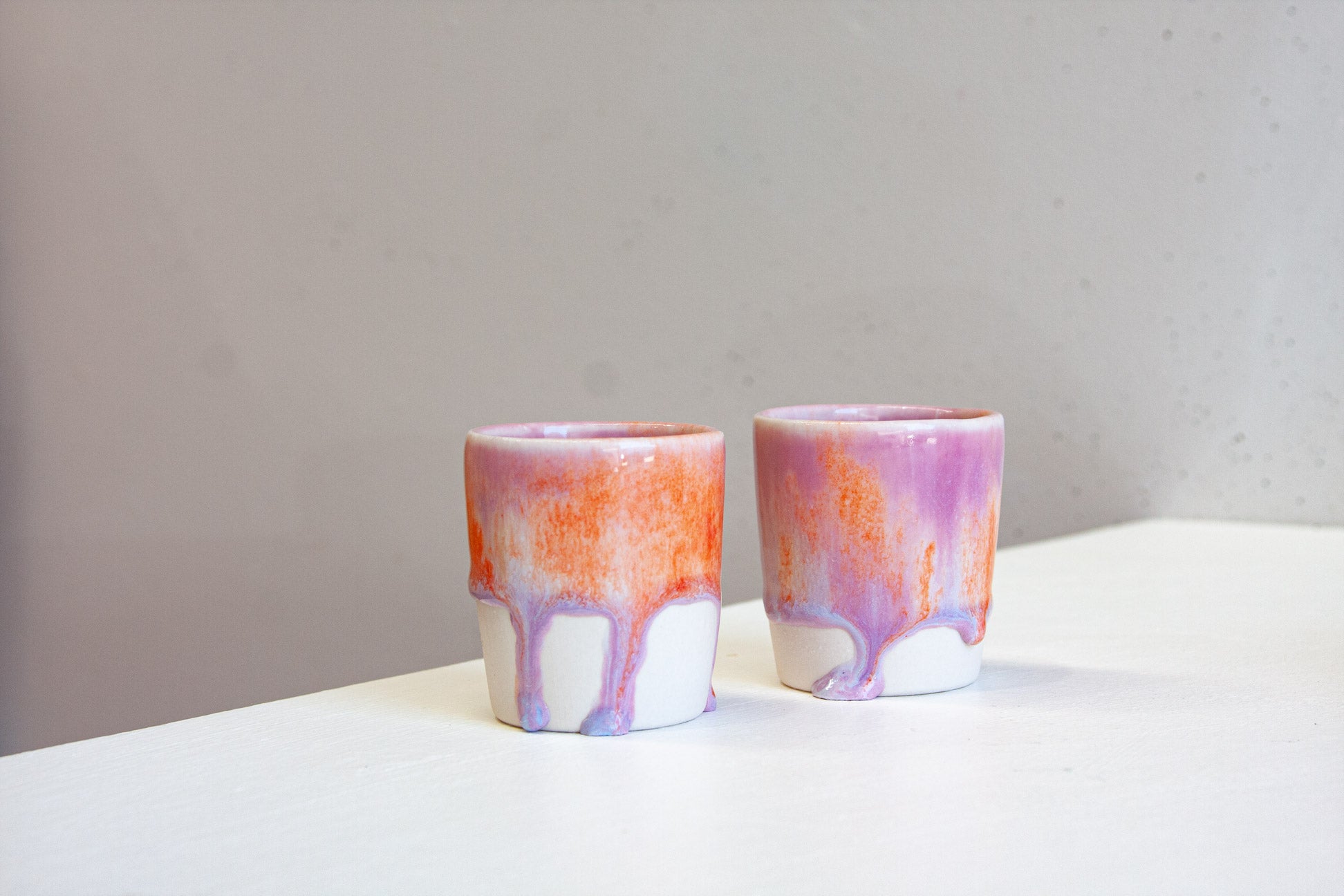 Two handmade ceramic espresso cups side by side, the purple and orange glaze dripping down to the bare white clay base.