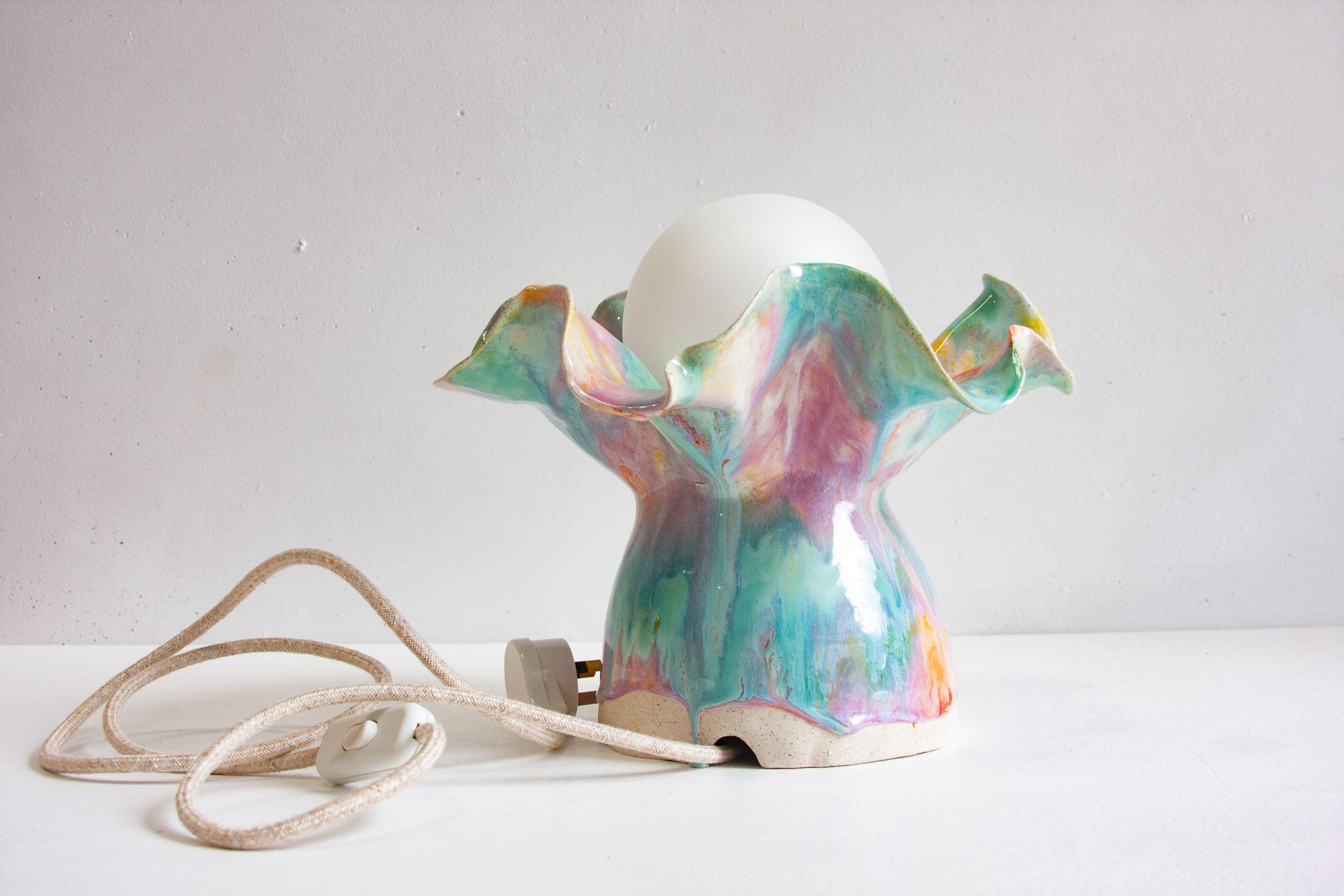 A handmade ceramic Oyster table lamp with its white linen cord and inline switch laid out beside it on a white surface.