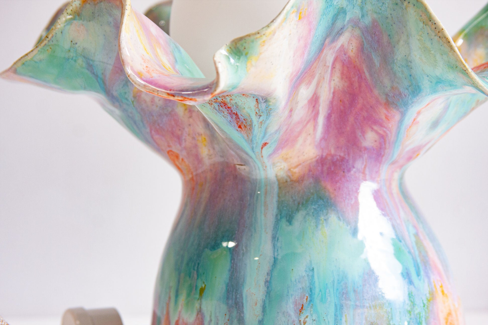Close-up of the ruffled ceramic base of a handmade Oyster table lamp, the glaze running through purple, green and orange.