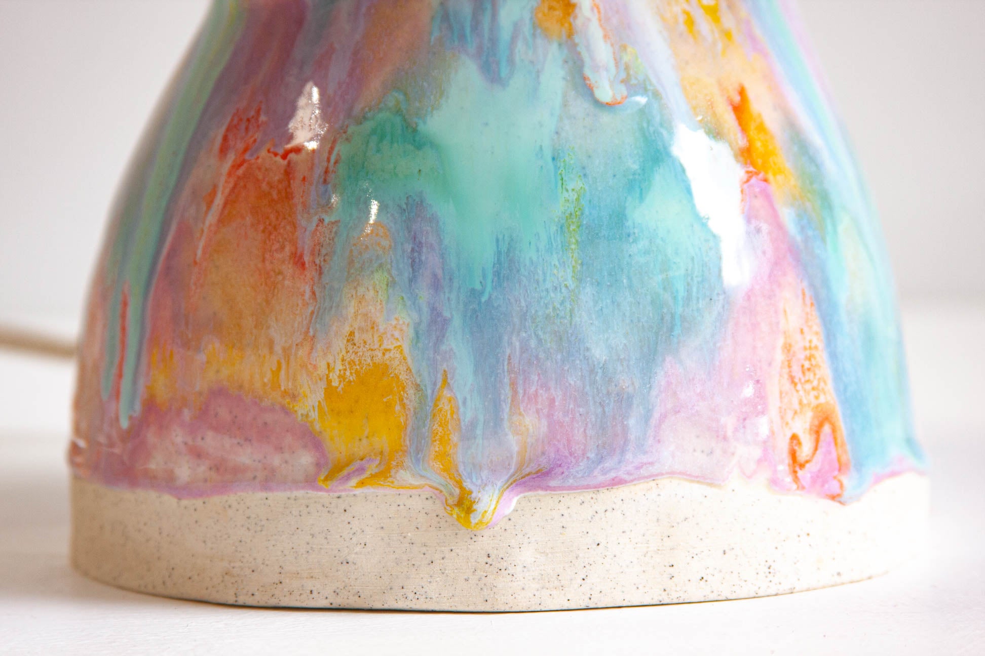 Close-up of the lower body of a handmade ceramic Oyster table lamp, the glaze running down in purple, green, orange and yellow to the bare clay foot.