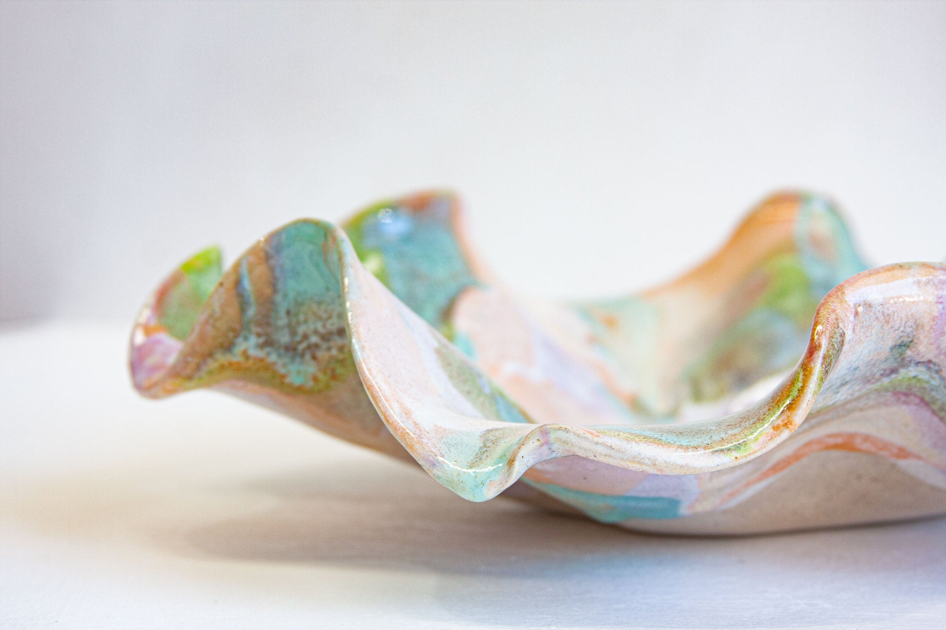 Close-up of the ruffled rim of a handmade ceramic oyster platter, the green and peach glaze following the folds of the form.