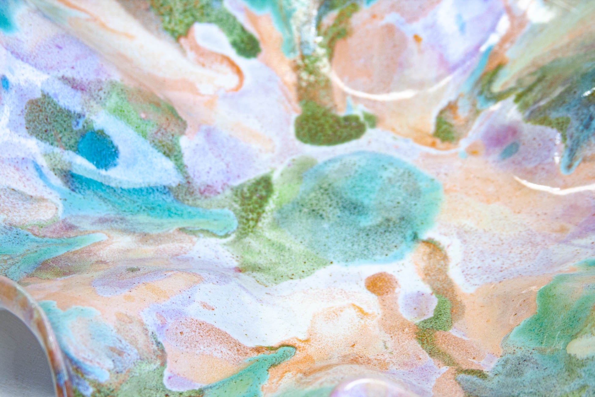Extreme close-up of the glazed surface, green and peach settling into soft hollows with purple and white between them.