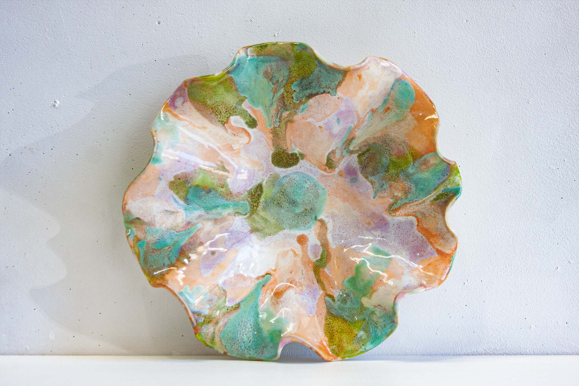A handmade ceramic oyster platter photographed flat from above, purple, green and peach pooling across the surface between white.