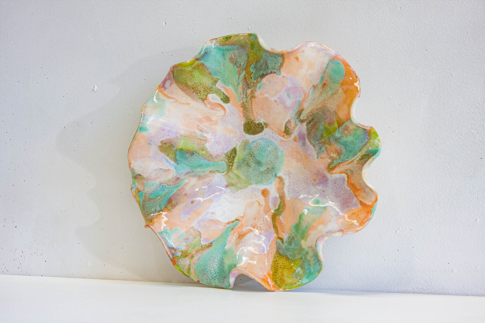 A handmade ceramic oyster platter seen from above at a slight angle, the scalloped edge framing purple, green and peach over white.