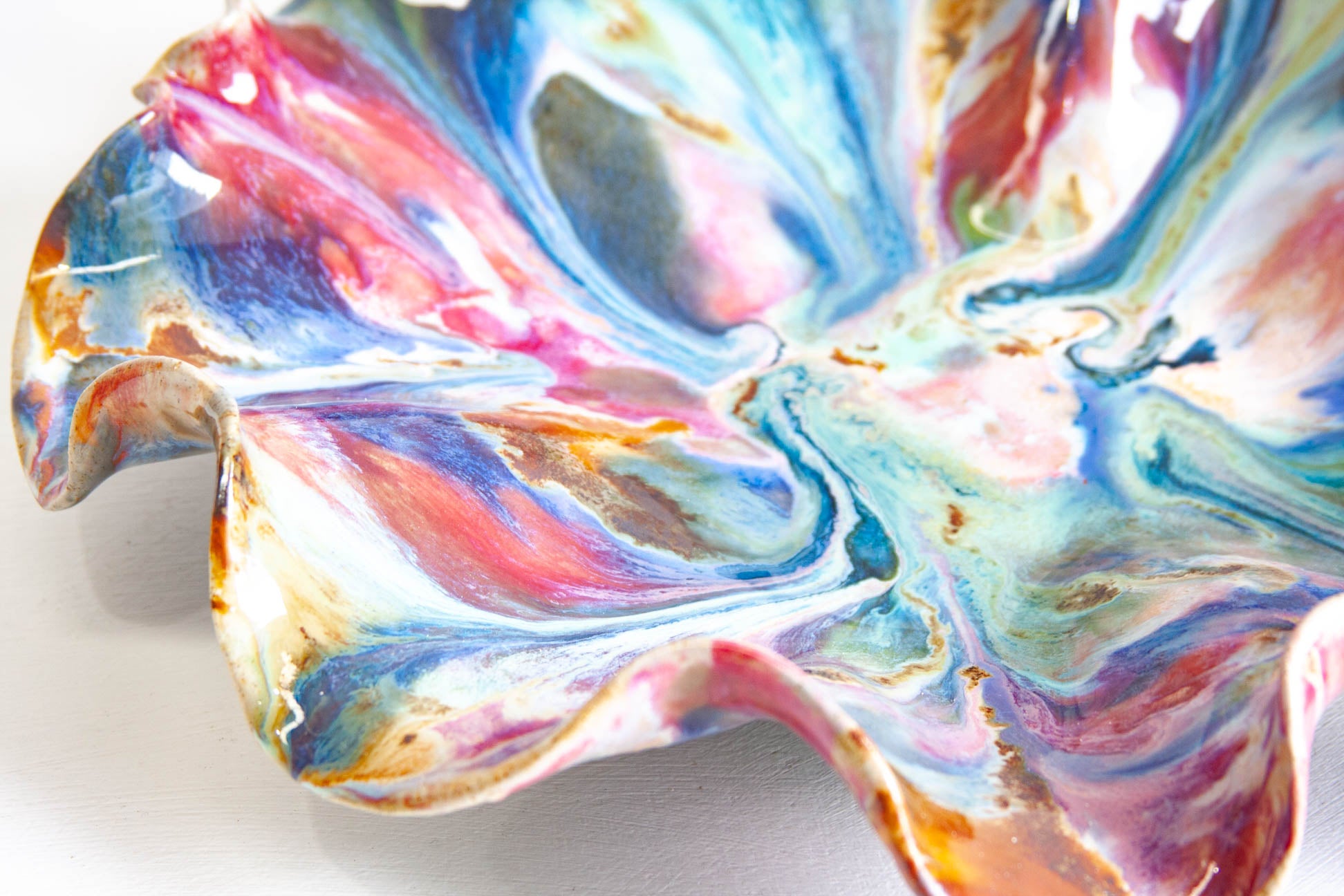 Close-up of the inside of a handmade ceramic oyster platter, the glaze streaming out from the centre in pink, blue, green and rust brown.