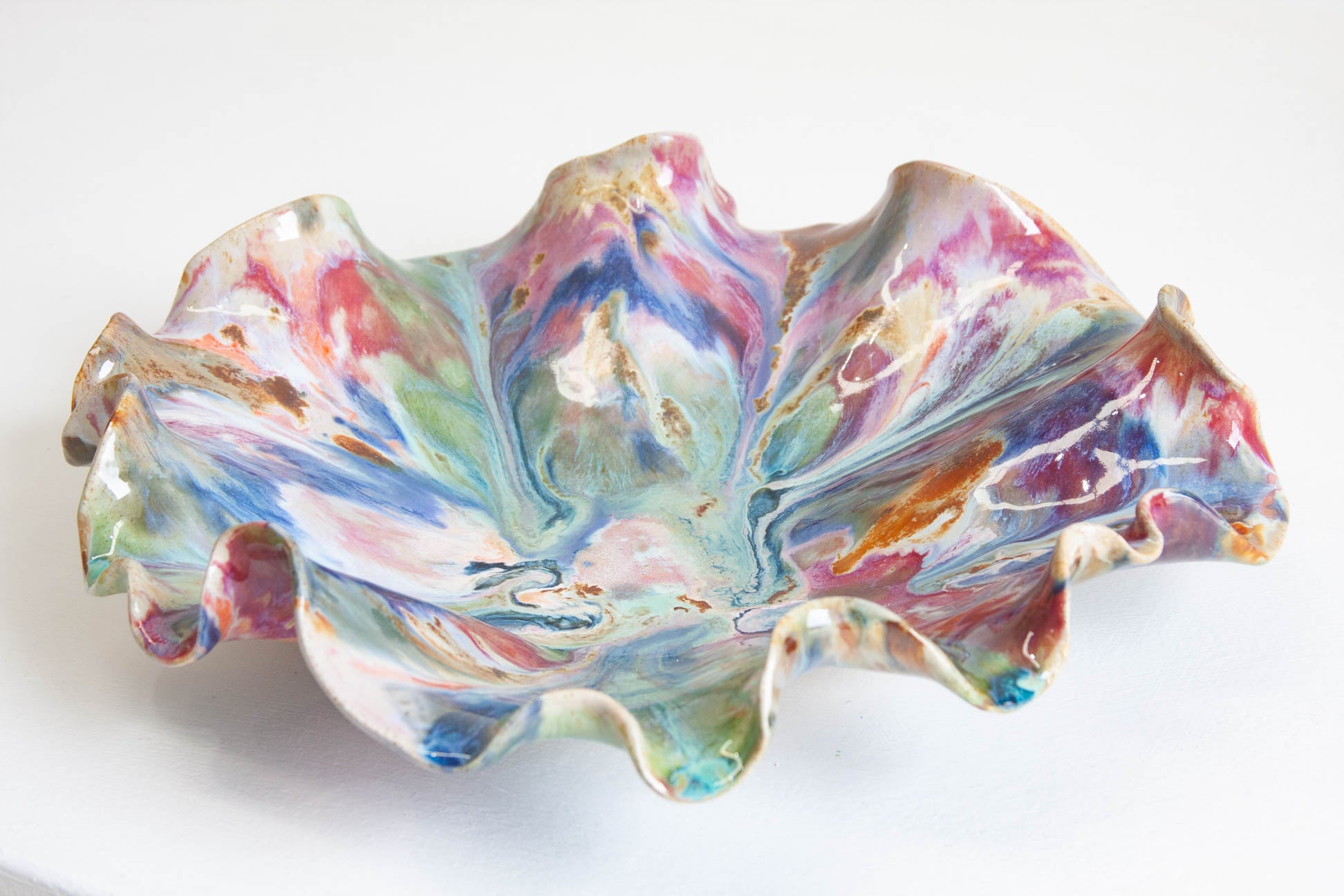 A handmade ceramic oyster platter seen from above at an angle, the ruffled rim and marbled pink, blue, green and brown glaze filling the frame.