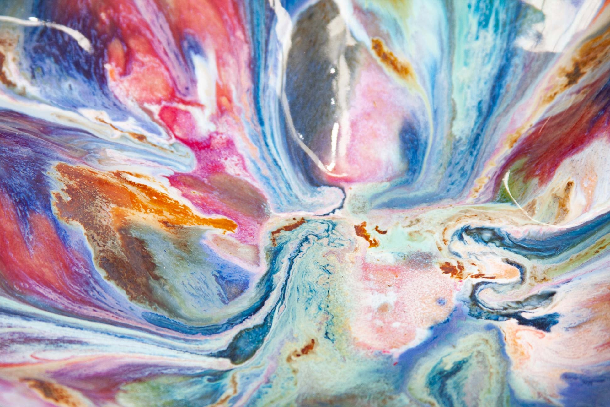 Macro view of the glazed surface of a handmade ceramic oyster platter, pink, blue, green and rust brown swirling together under a glossy finish.