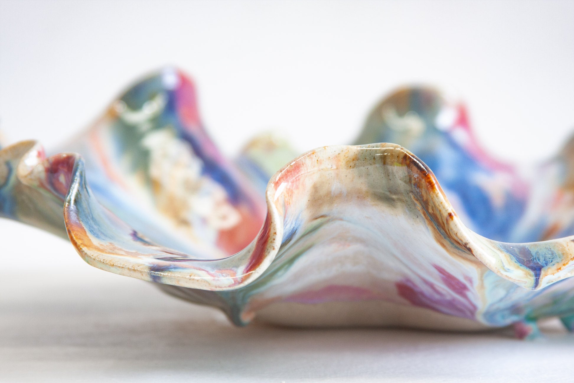 Side view of a handmade ceramic oyster platter, the deep ruffled folds marbled in pink, blue, green and brown.