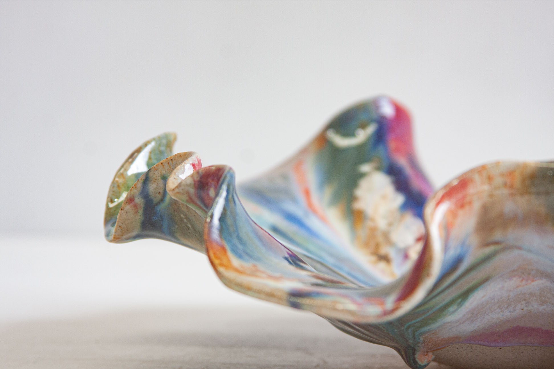 A handmade ceramic oyster platter seen from the side, one pointed fold lifting away from the shallow marbled dish.