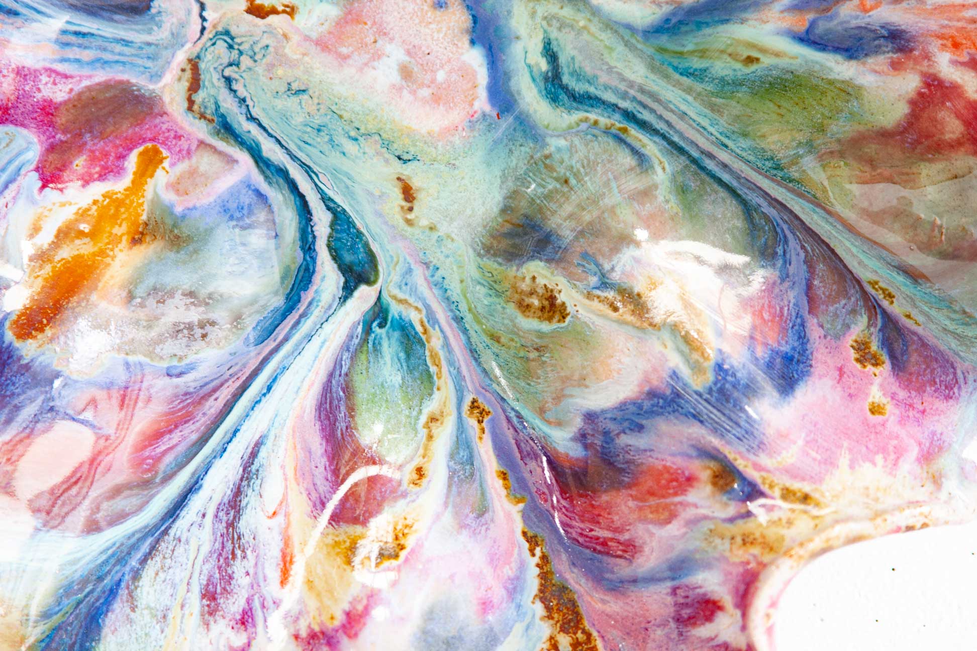 Macro detail of the glaze on a handmade ceramic oyster platter, veins of blue, pink, green and rust brown running across a pale ground.