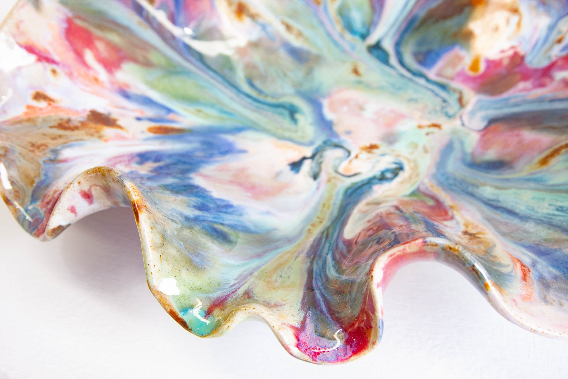 Close-up of a handmade ceramic oyster platter from above, the glaze marbling through pink, blue, green and brown out to the ruffled rim.