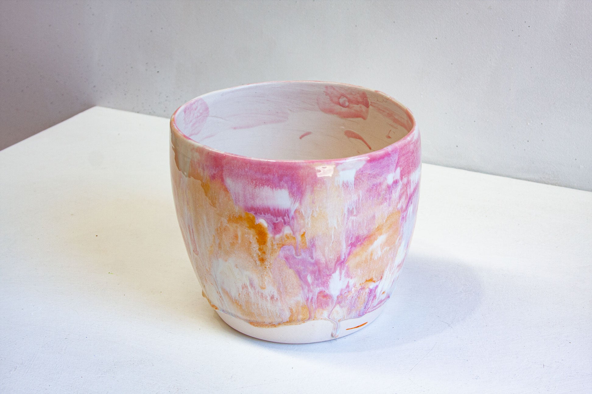 A handmade ceramic large planter glazed in pink, cream, peach and white, seen from above and to one side with its slightly oval rim.