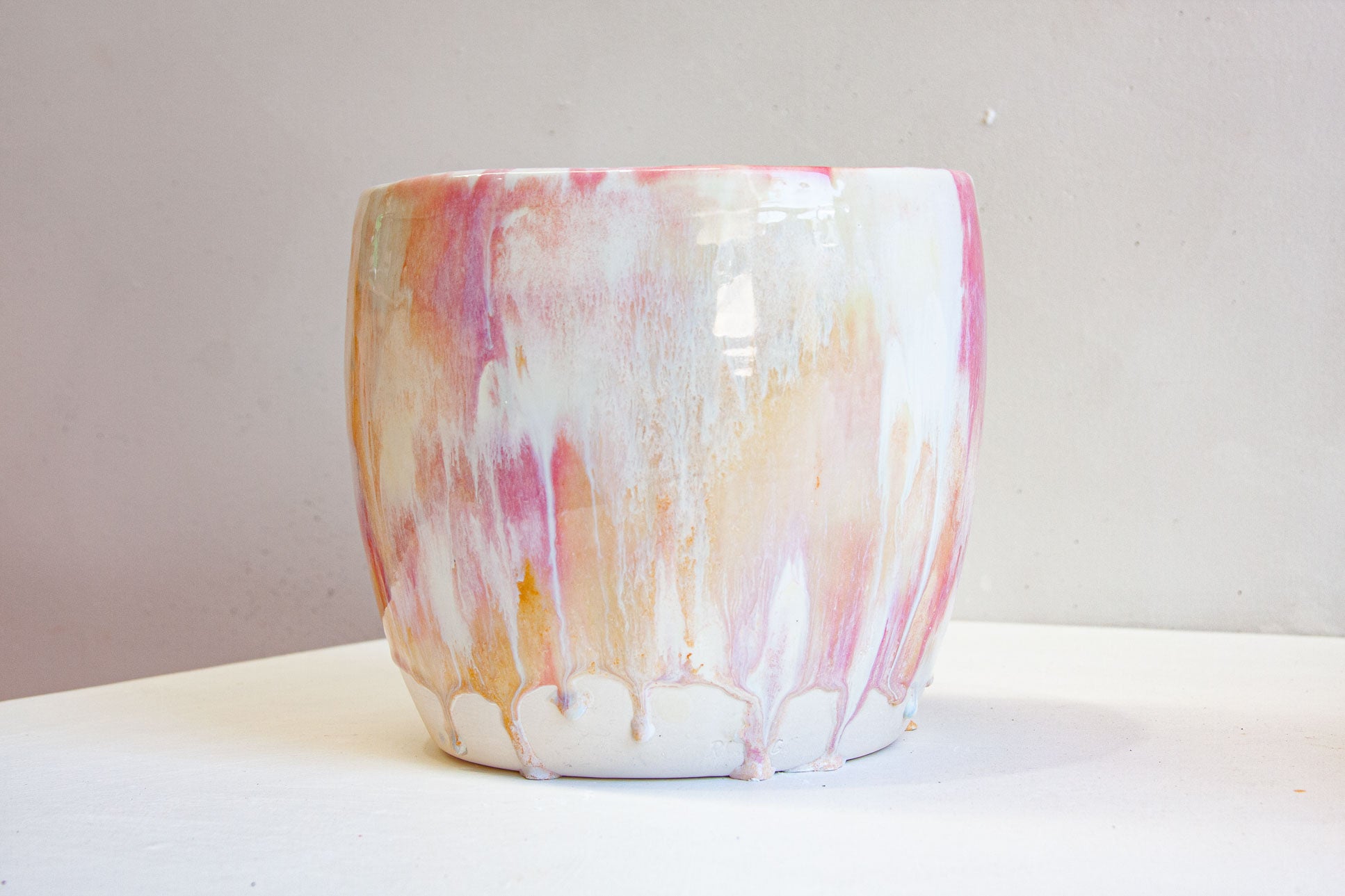 A handmade ceramic large planter seen from the front, pink and peach washing down over cream and white into soft drips above the foot.