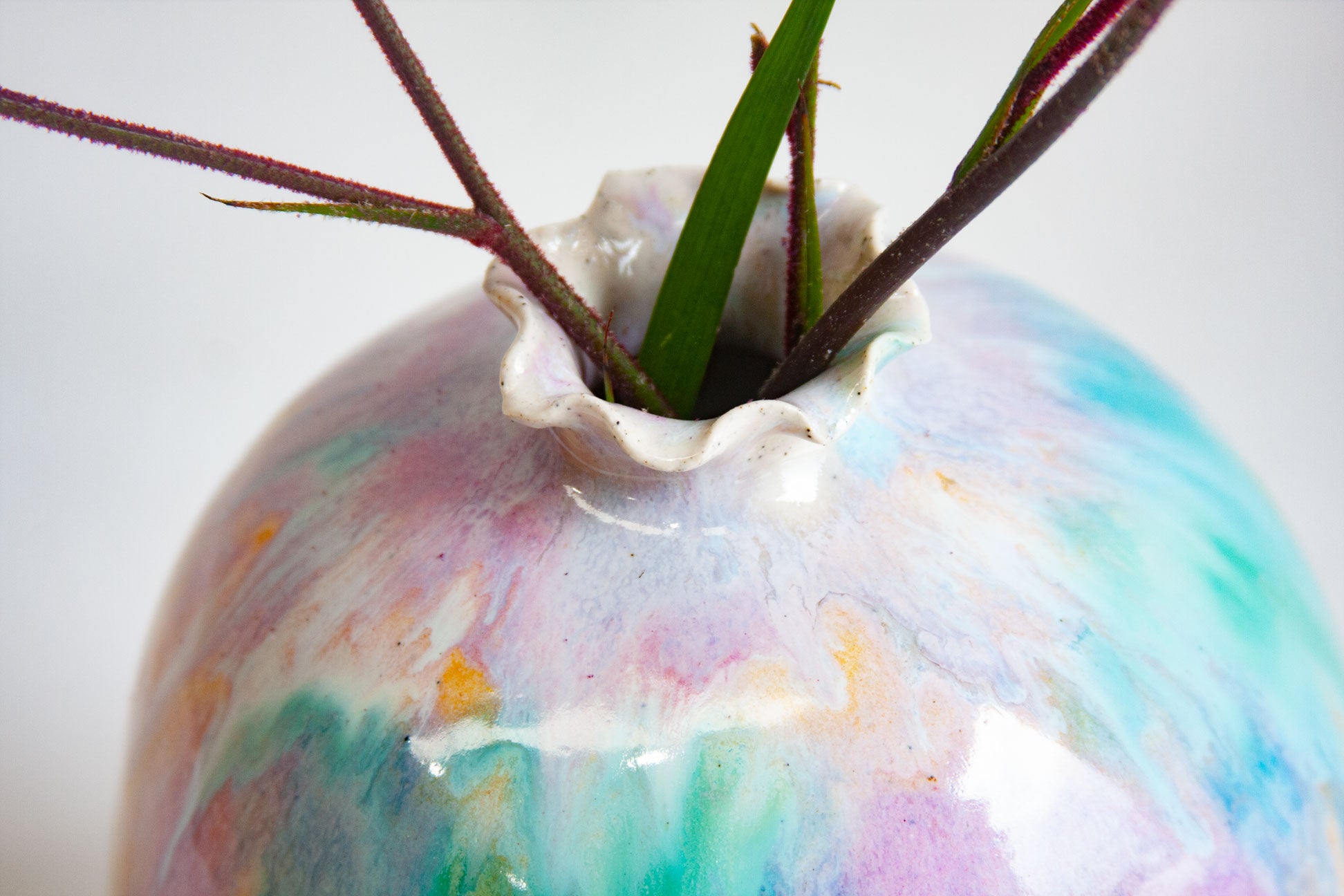 Close-up of the top of a handmade ceramic sculptural vase, green and purple washing down from the frilled neck with peach breaking through.