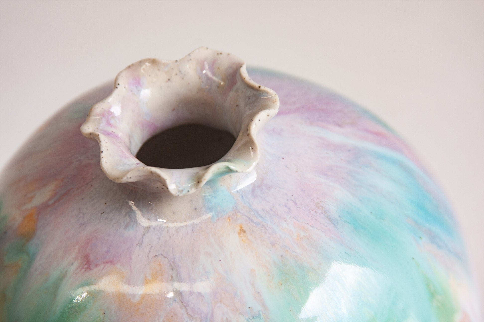 Close-up of the frilled neck of a handmade ceramic sculptural vase, the glaze gathering in pale purple and green around the opening.