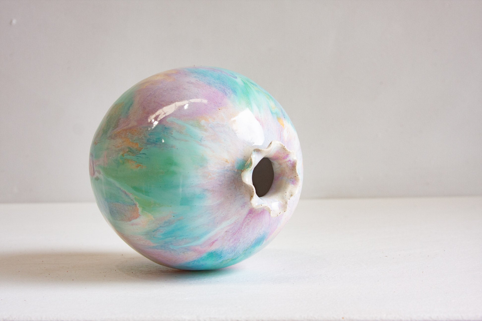 A handmade ceramic sculptural vase lying on its side, showing the frilled opening and the glaze washing across the round body.