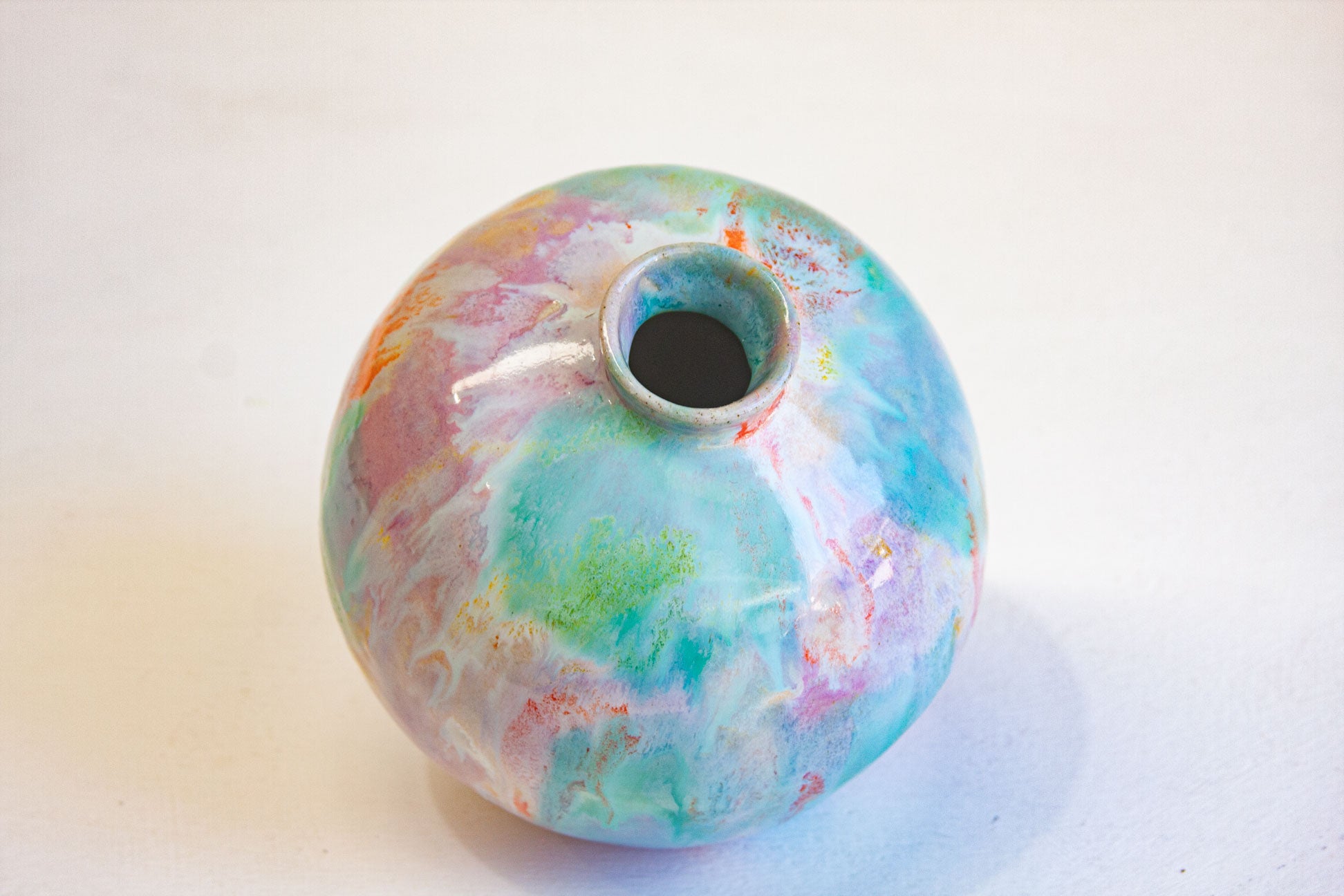Looking down onto a round handmade ceramic vase, showing the narrow neck opening and the purple, green and orange glaze across the shoulder.