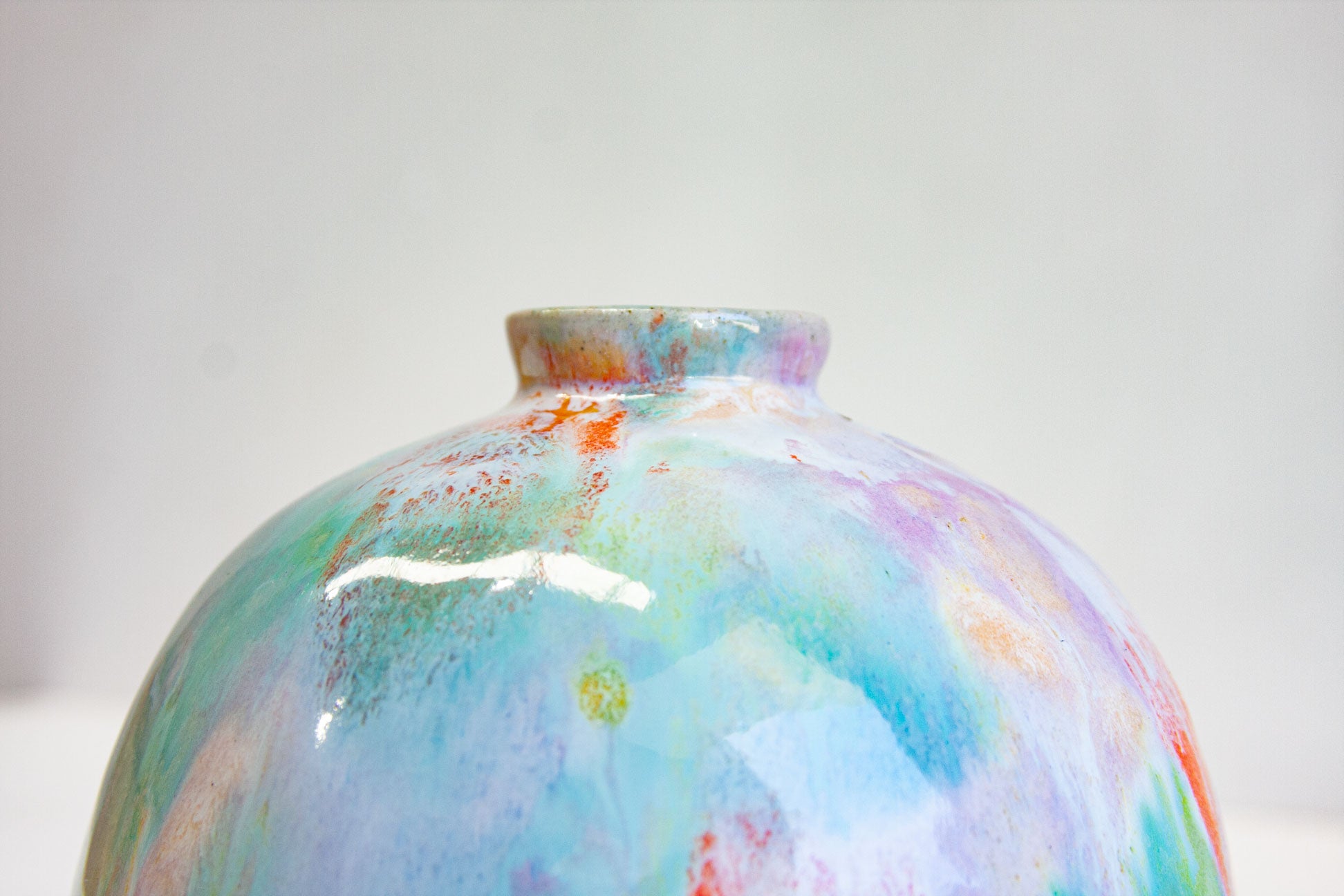 Close-up of the upper half of a round handmade ceramic vase, purple and green meeting flecks of orange around the narrow neck.
