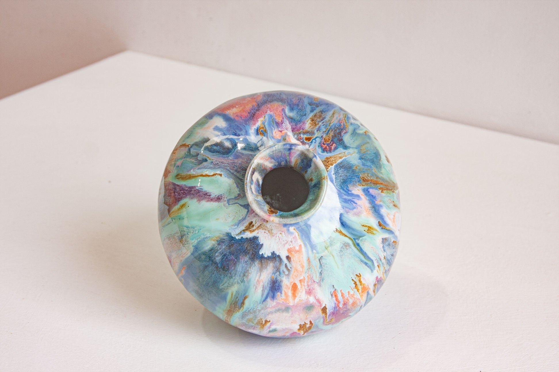 Looking down onto a large round handmade ceramic vase, showing the small neck and the marbled blue, pink and ochre glaze over the shoulder.