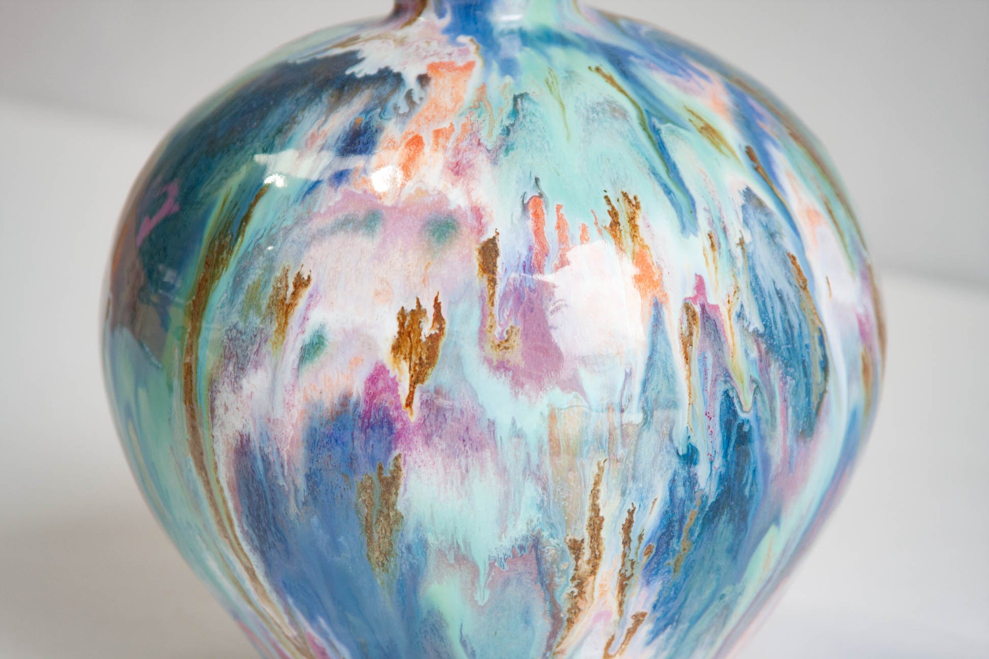 Close-up of the body of a handmade ceramic vase, blue, teal, pink and white streaked through with ochre.