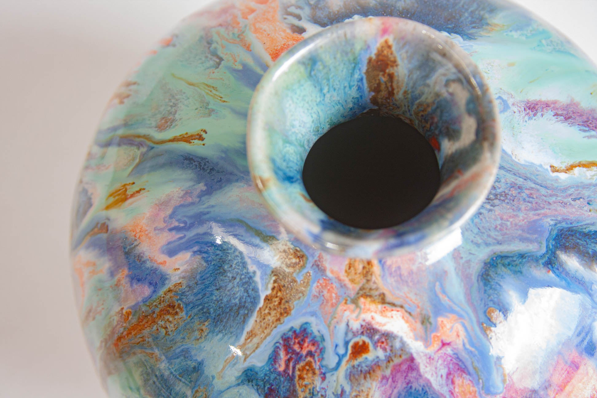 Extreme close-up of the vase's neck opening, the glaze marbled in blue, teal, pink, white and ochre across the shoulder.