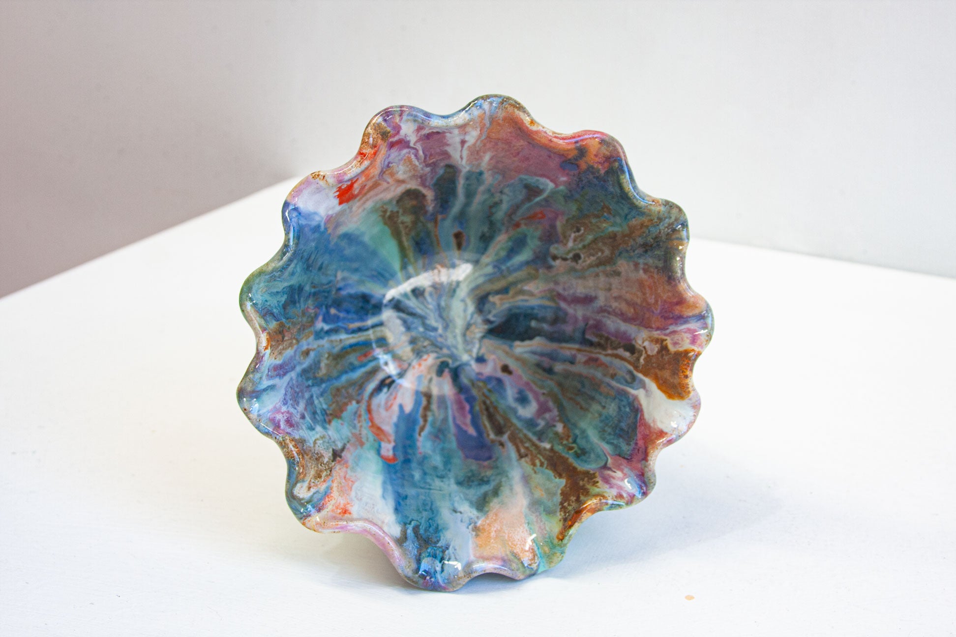 Looking down into a handmade ceramic frill vessel, the glazed interior streaming out from the centre in blue, teal, purple and rust inside the frilled rim.