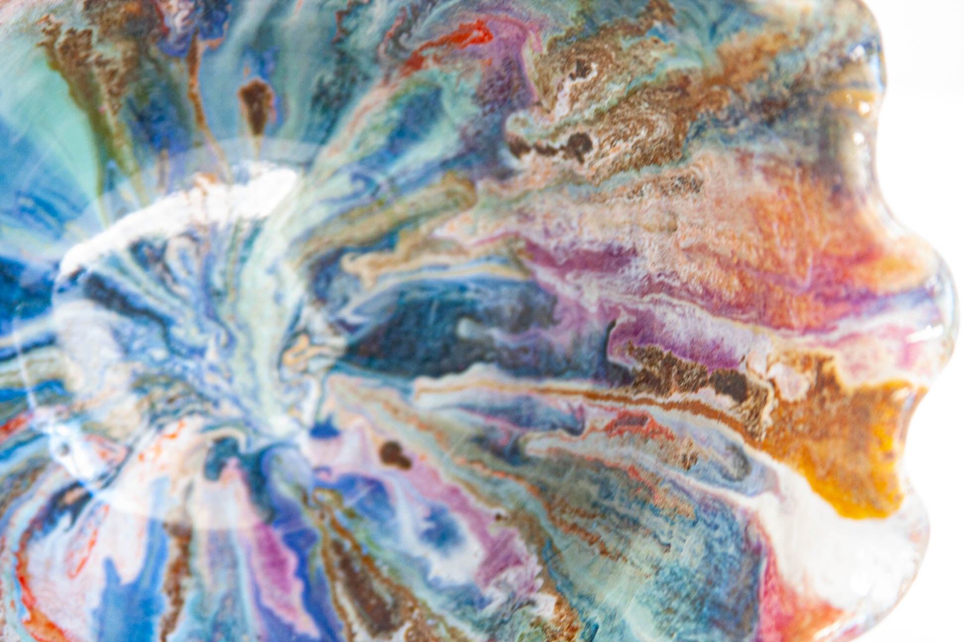 Close-up inside a handmade ceramic frill vessel, the glaze radiating from the centre in blue, teal, purple, pink and rust under a glossy surface.
