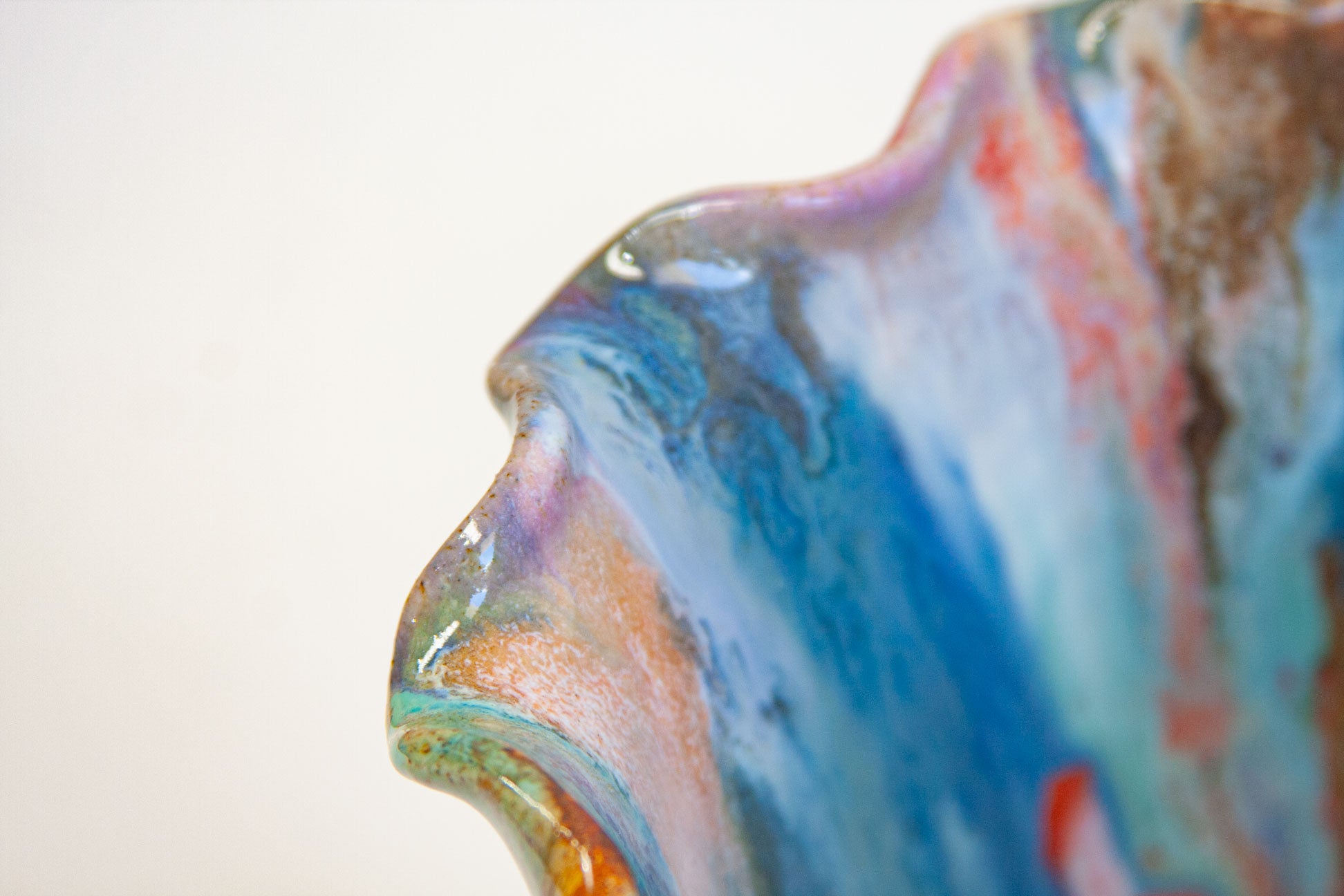 Close-up of the frilled rim of a handmade ceramic frill vessel, blue, teal, purple and rust gathering along every fold.