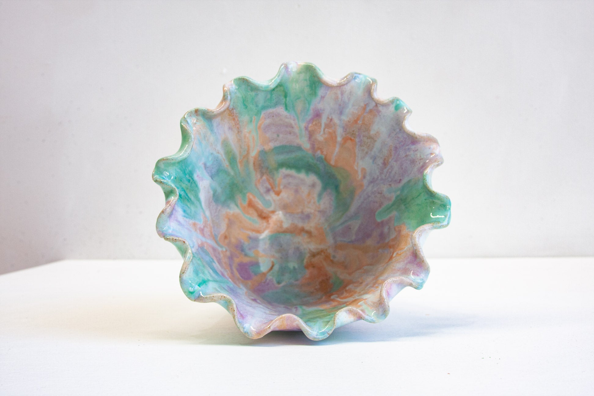 Looking into a handmade ceramic frill vessel at an angle, green and peach sweeping across the glazed interior below the frilled rim.
