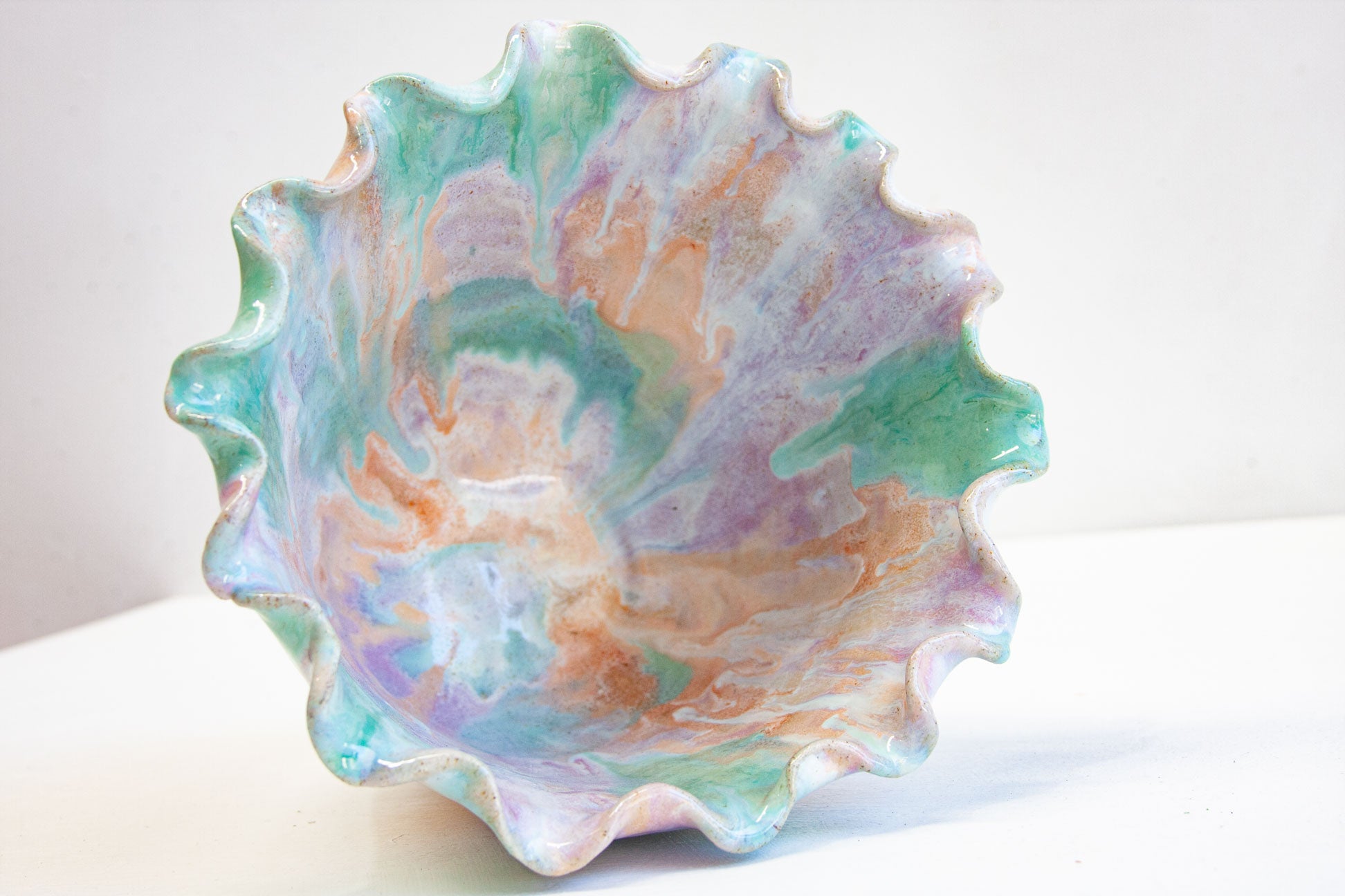Looking down into a handmade ceramic frill vessel, the glazed interior swirling through pastel purple, peach and green inside the frilled rim.