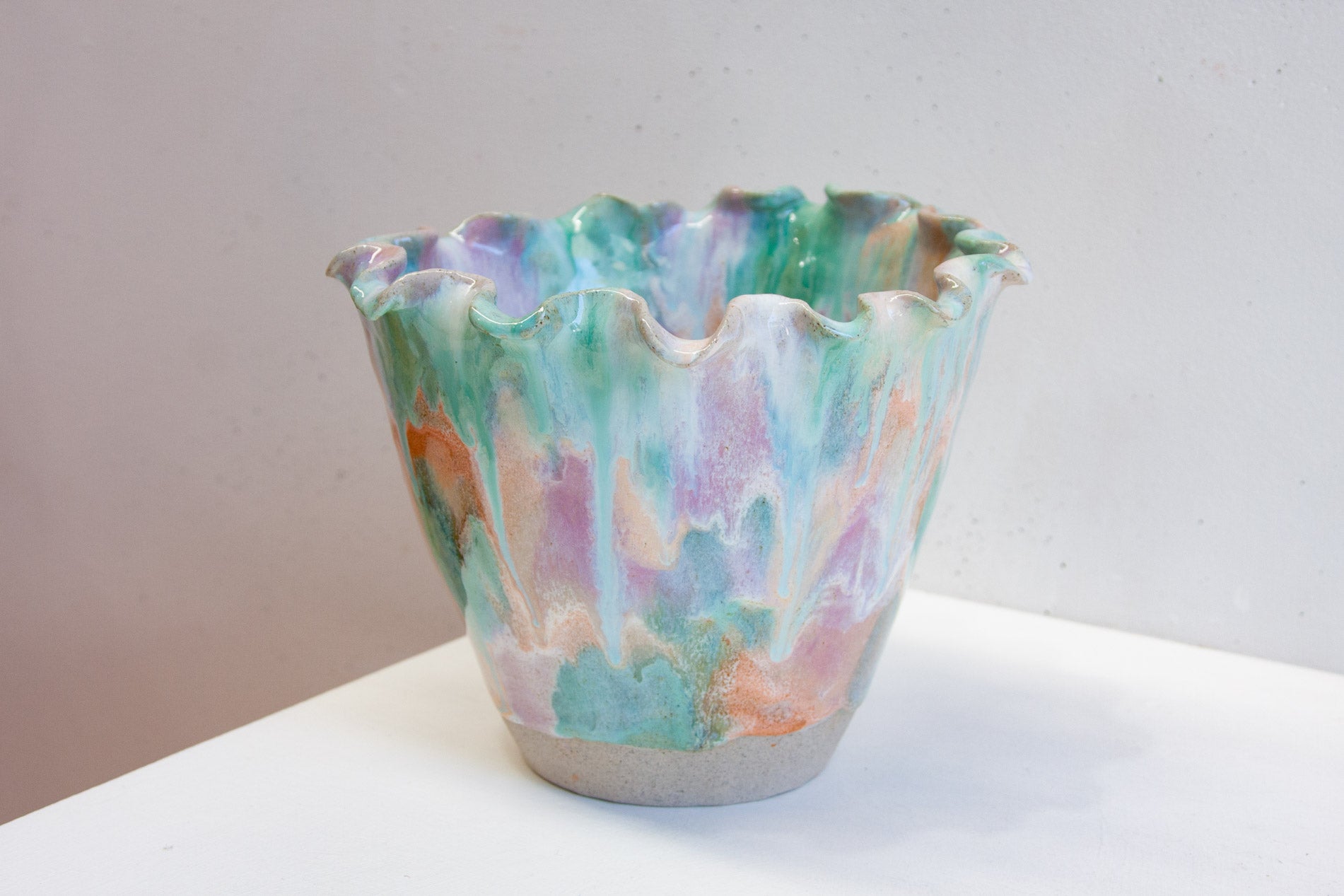 Close-up of the glaze on a handmade ceramic frill vessel, peach and green running in soft vertical streaks over pale purple.
