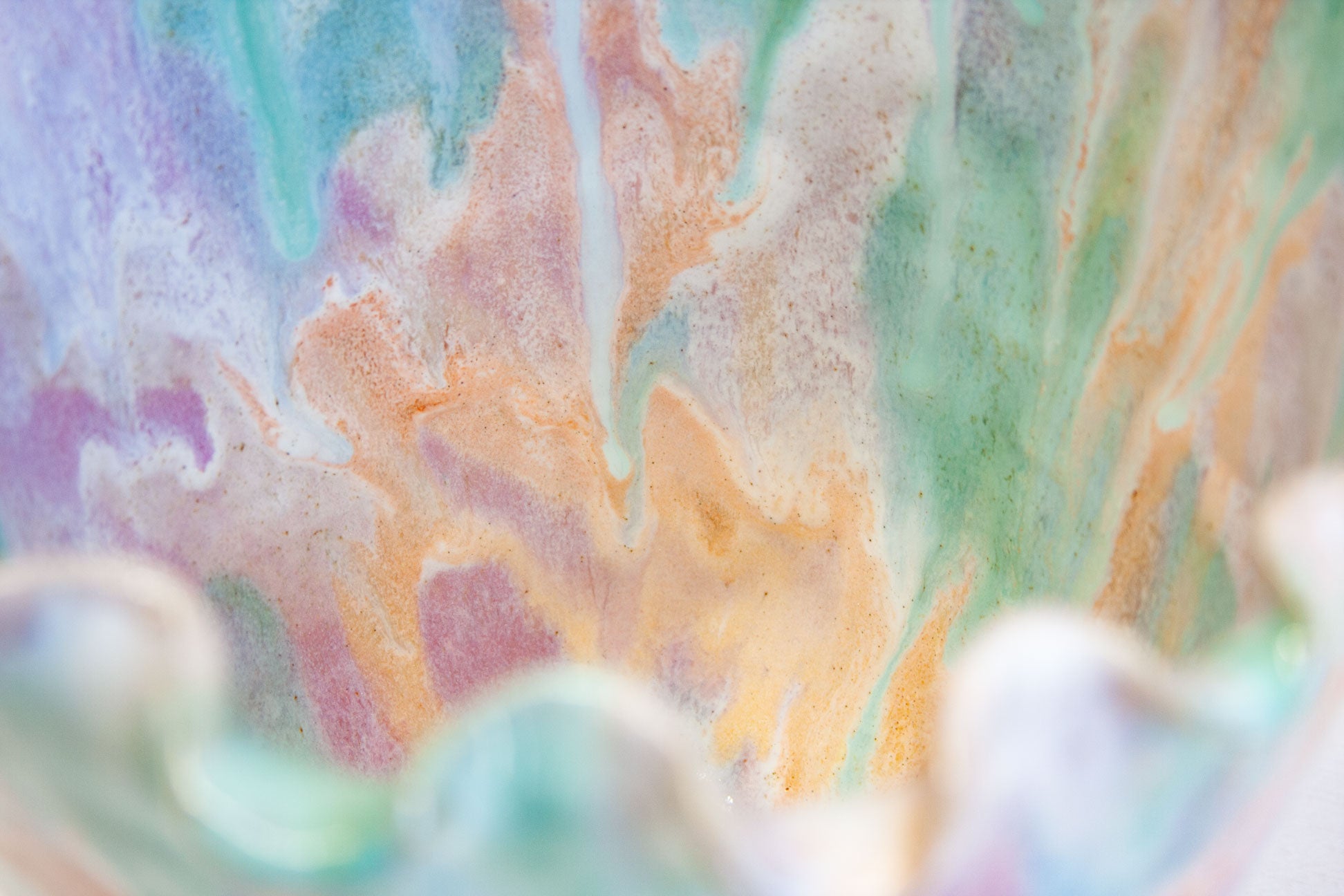 Close-up of the frilled rim of a handmade ceramic frill vessel, the glaze gathering along every fold in green, purple and peach.