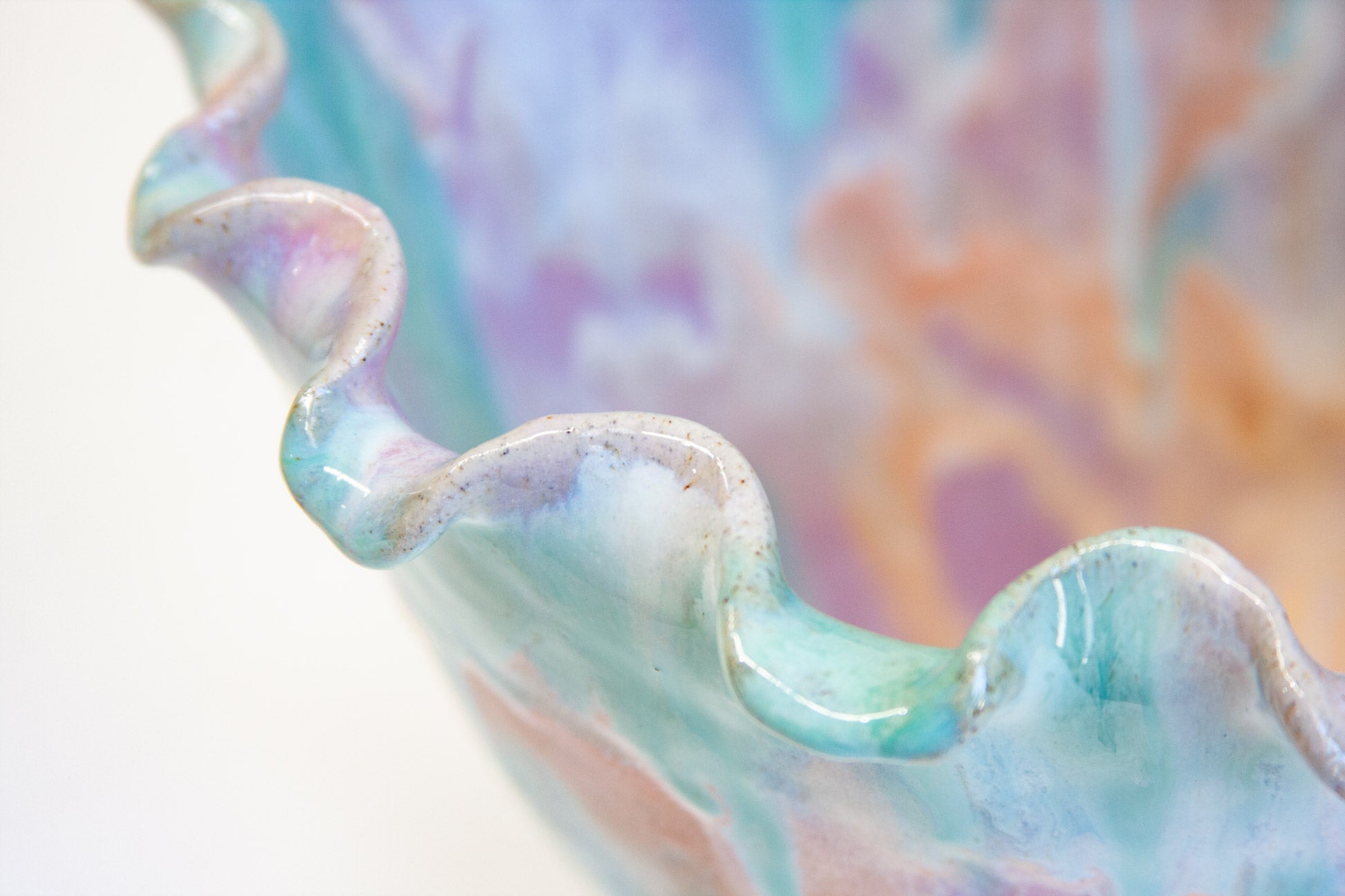 A handmade ceramic frill vessel seen from the front, pastel purple, peach and green running down the flared sides to a bare white clay foot.