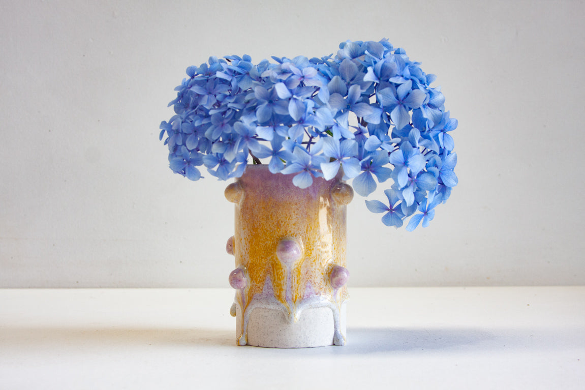 handmade ceramic bauble vase glazed in yellow and purple with blue hydrangea in it